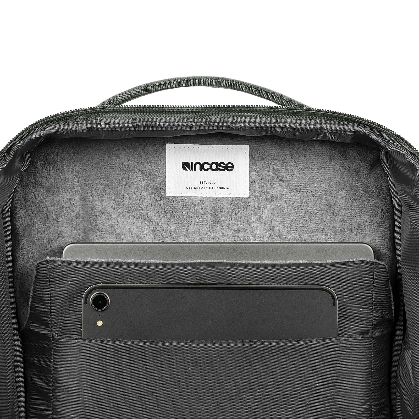 Im Inneren eines Rucksacks. In einer Tasche befinden sich ein schwarzes Telefon und ein Laptop. Das Incase-Logo ist sichtbar.