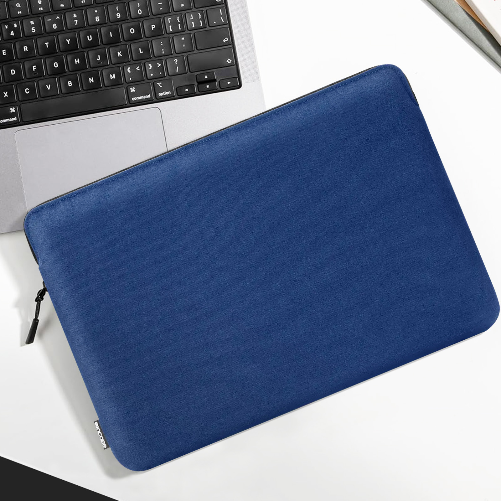 Custodia blu per laptop su una superficie bianca accanto a una tastiera per laptop. Ha una cerniera nera.