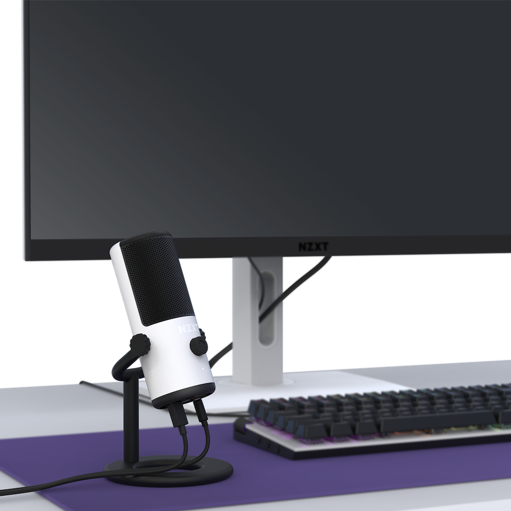 Biały i czarny mikrofon na statywie. Monitor w tle, klawiatura i podkładka na biurku.