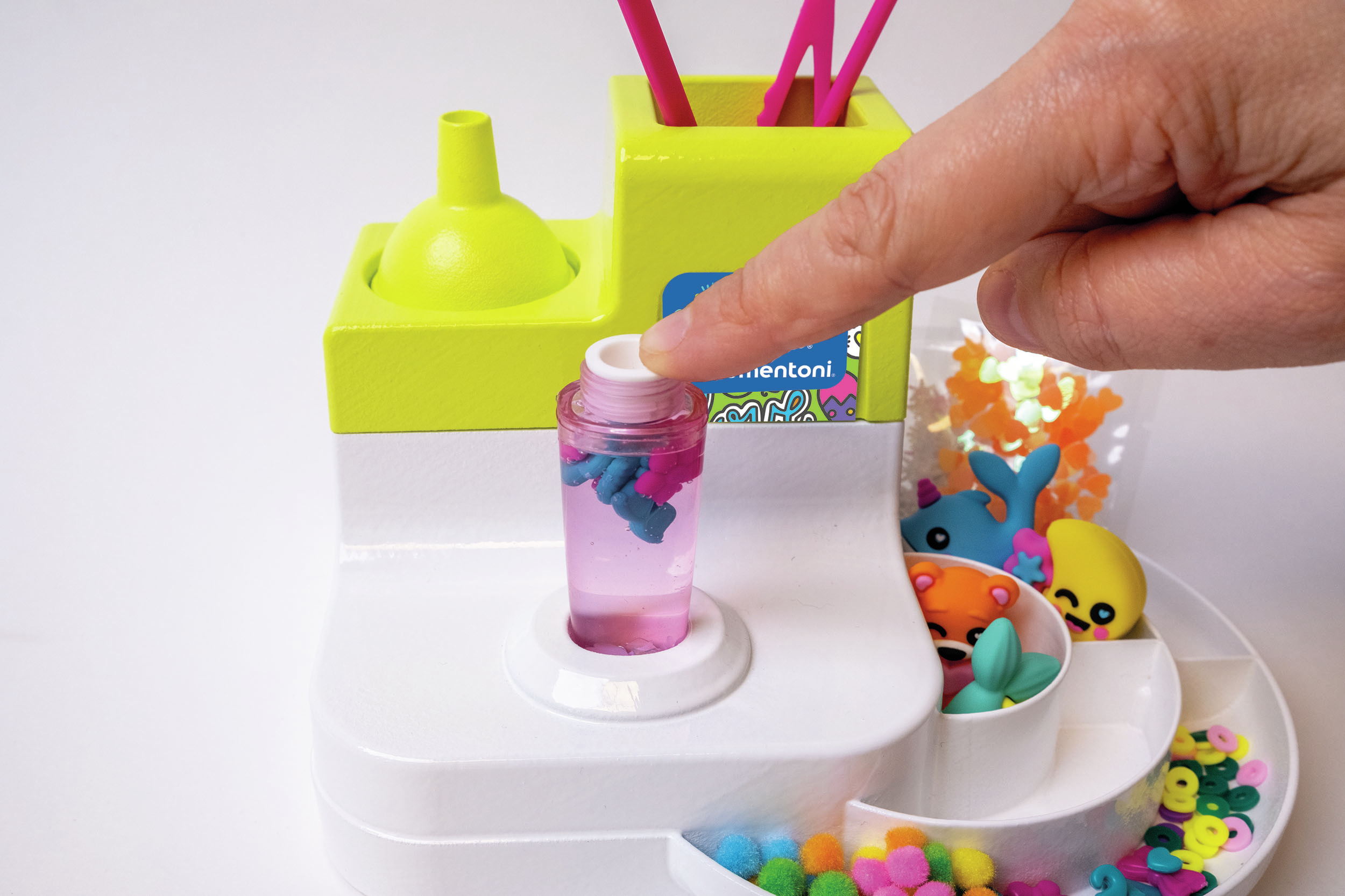 Ręka naciskająca przycisk na zestawie rzemieślniczym. Obecne kolorowe elementy i małe zabawki.