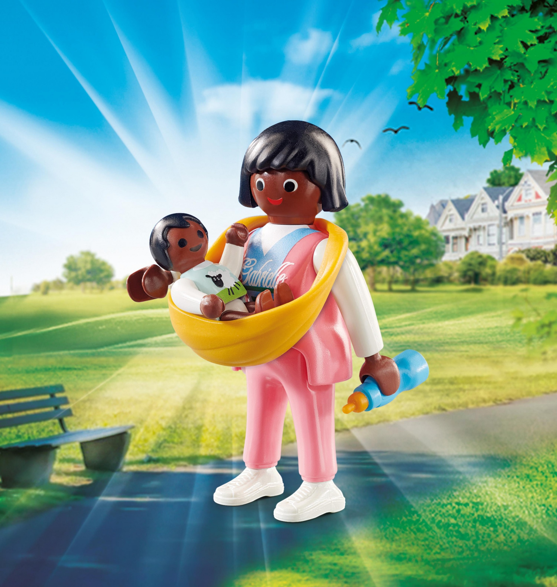 Figura Playmobil di una donna che tiene un bambino in un marsupio giallo, con un biberon, in un ambiente parco. Soleggiato, luminoso.
