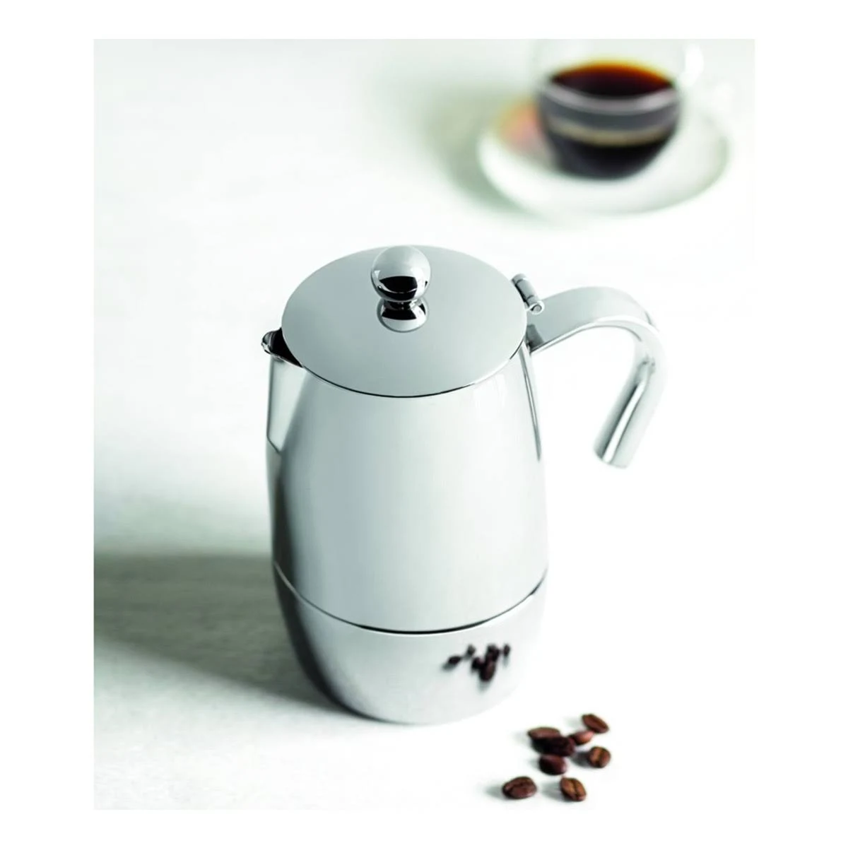 Caffettiera argentata lucida su superficie bianca. Chicchi di caffè e tazza sullo sfondo.