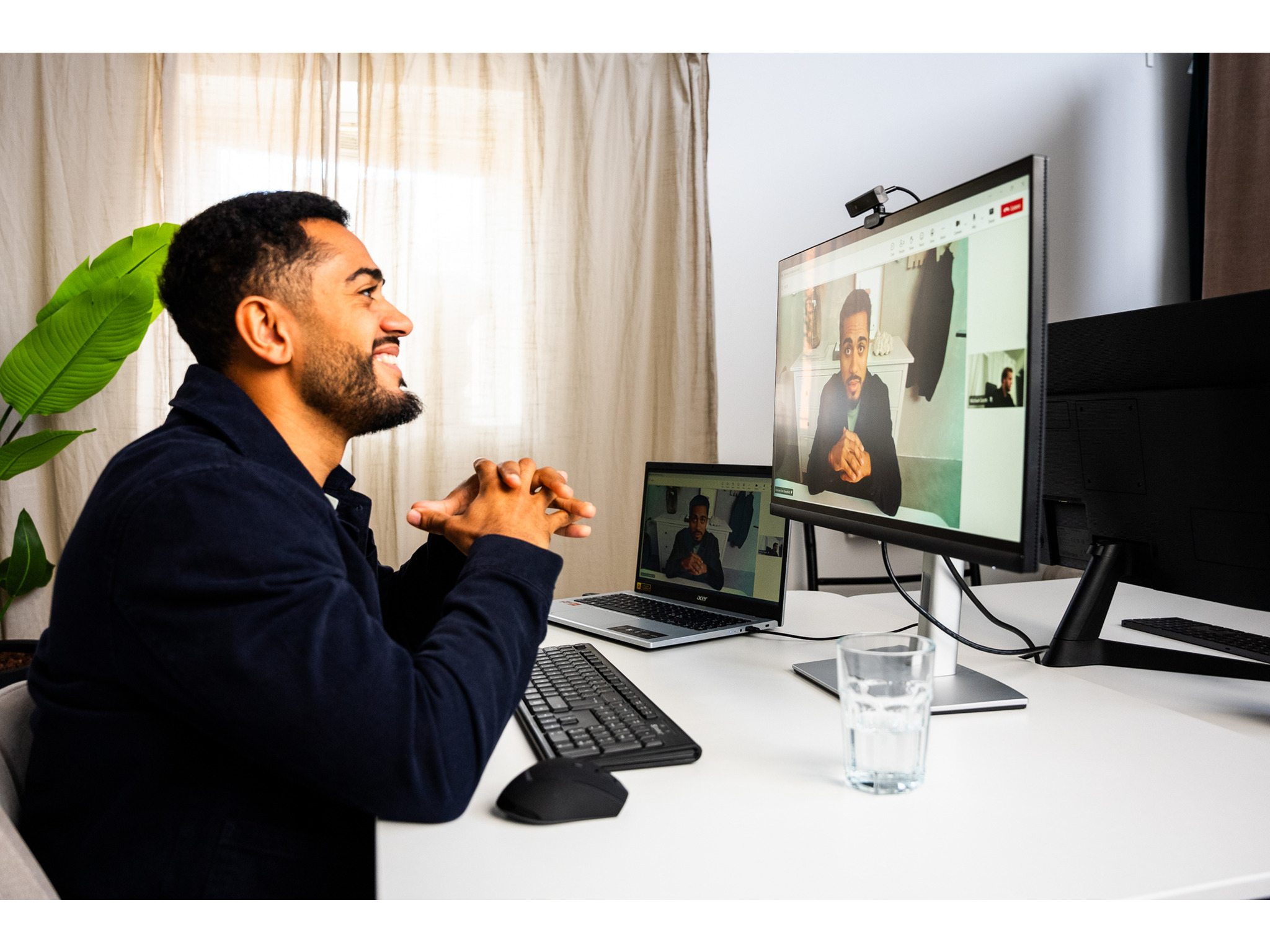 Mężczyzna w rozmowie wideo, uśmiechnięty i gestykulujący, z kamerą internetową na monitorze.