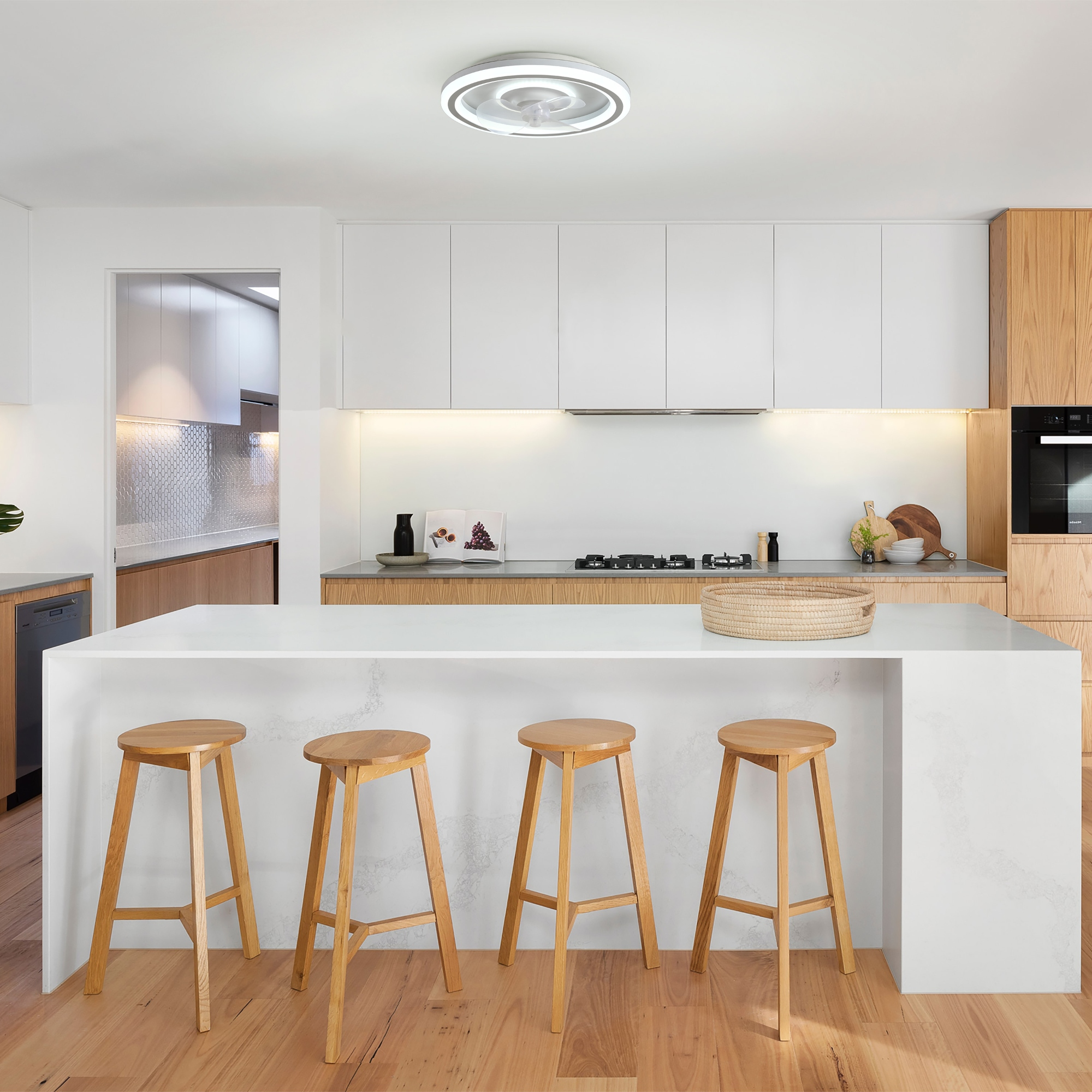 Cocina moderna con gabinetes blancos, detalles en madera, isla con taburetes y una lámpara de techo empotrada.
