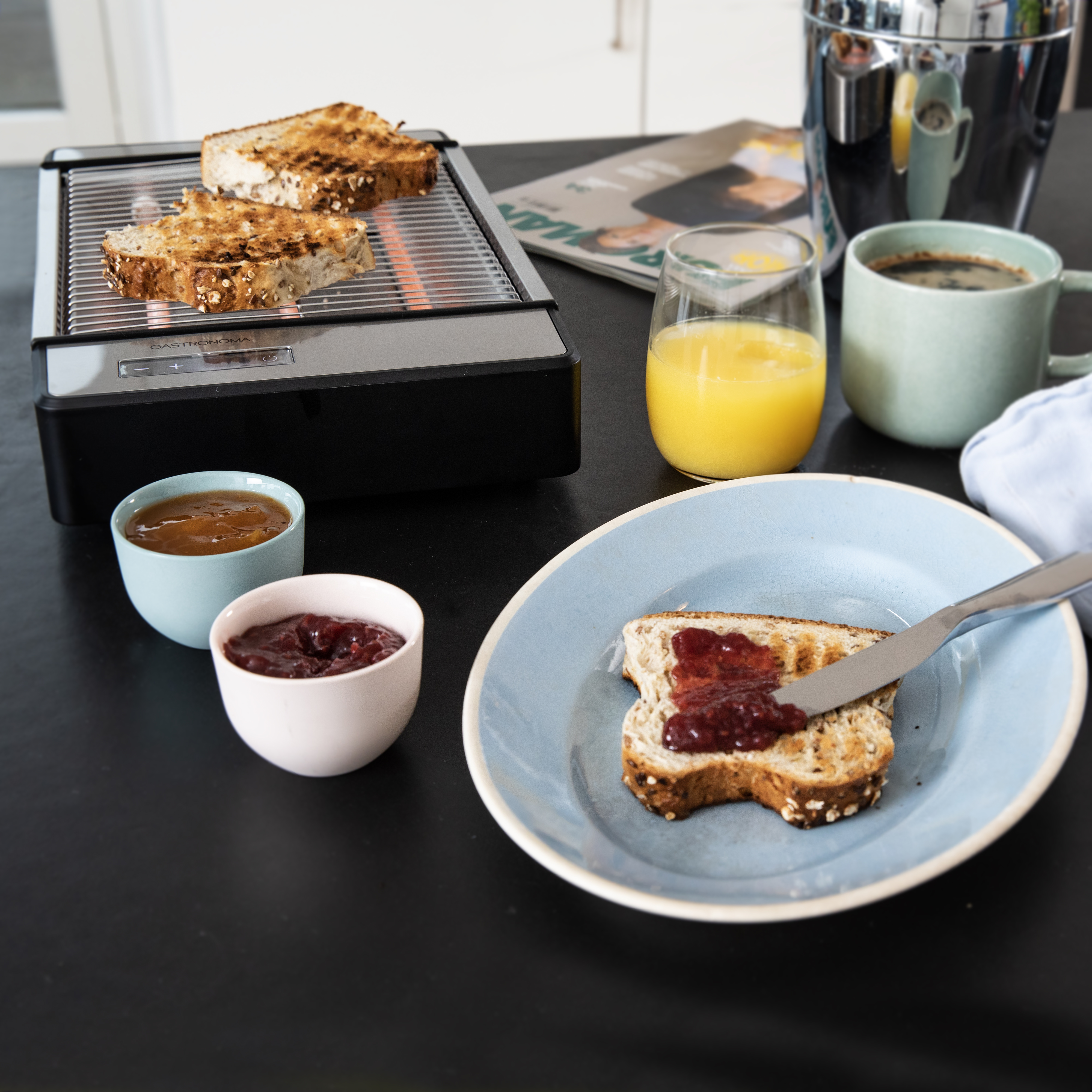 Scena śniadaniowa: Tosty, dżem, sok pomarańczowy, kawa. Toster po lewej.