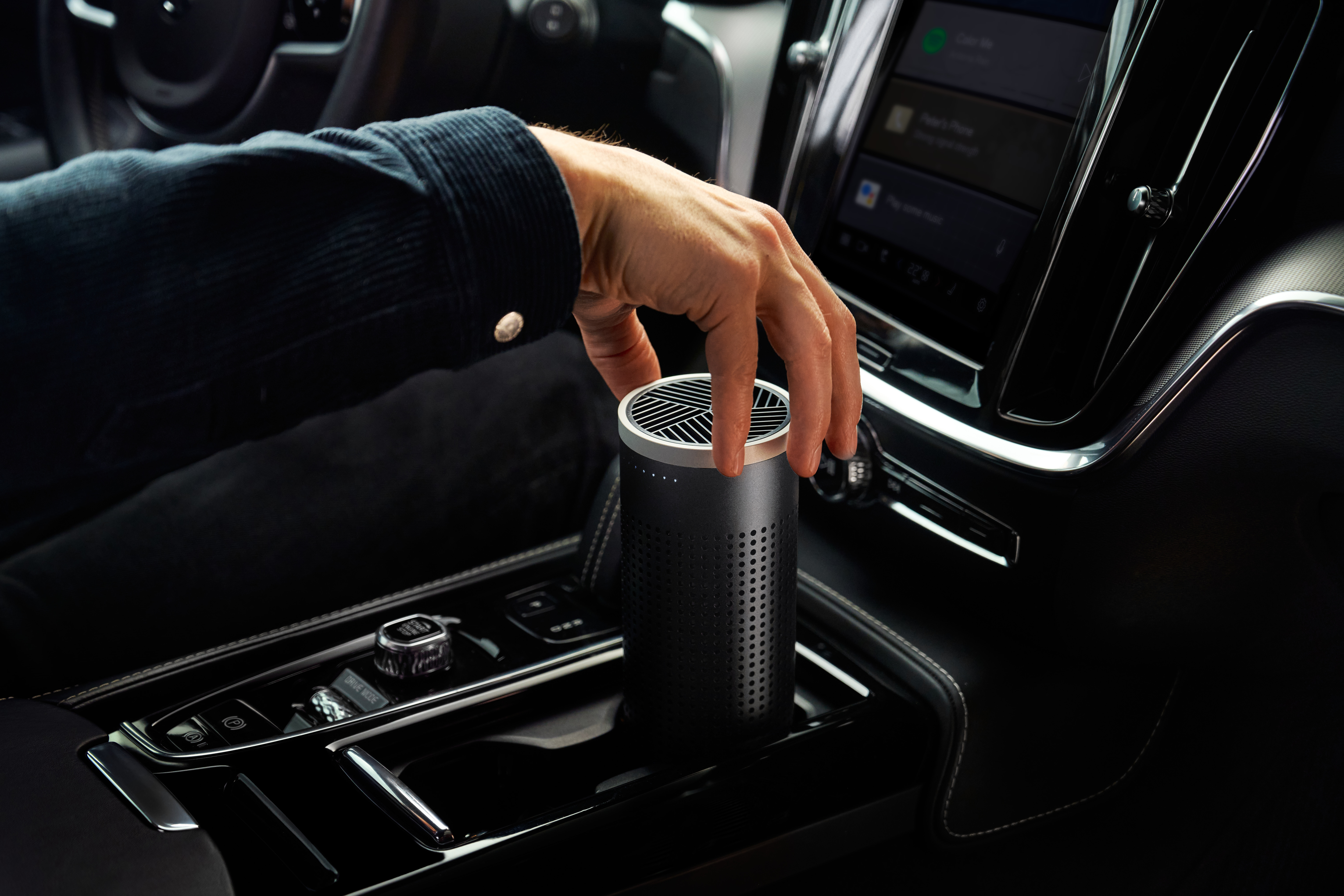 Hand greift nach einem schwarzen Luftreiniger in der Autokonsole, neben Gangschaltung und Infotainment.