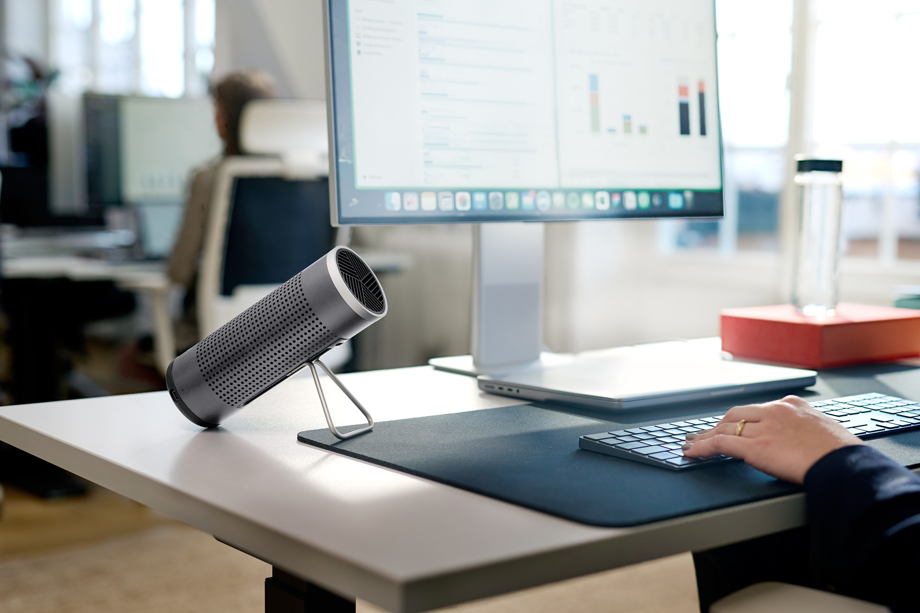 Büro mit Schreibtisch, Monitor, Tastatur und Luftreiniger. Die Hand einer Person liegt auf der Tastatur.