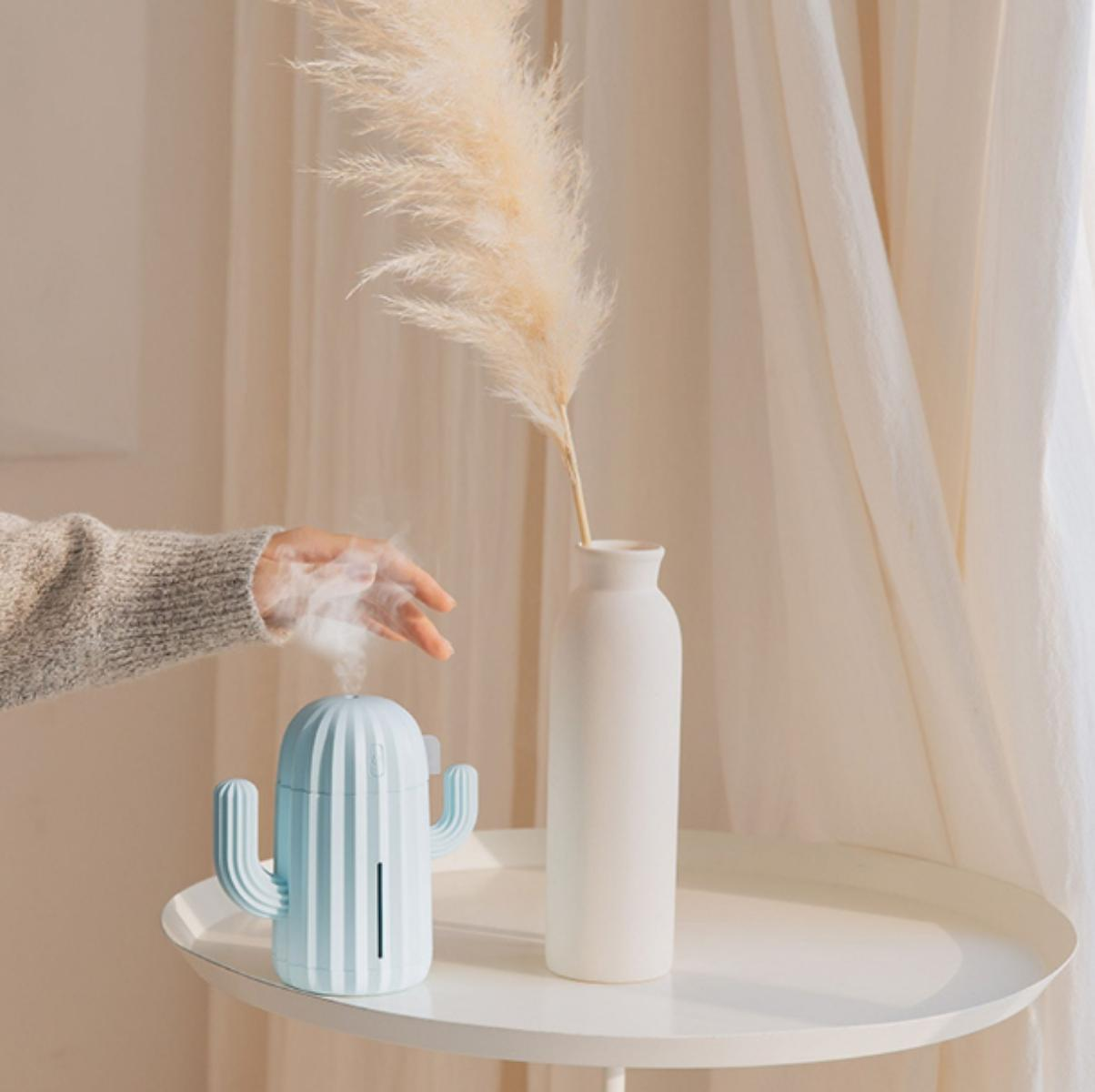 Ein blauer Kaktus-Luftbefeuchter, der Dampf abgibt, auf einem Tisch, mit einer Vase mit Pampasgras.