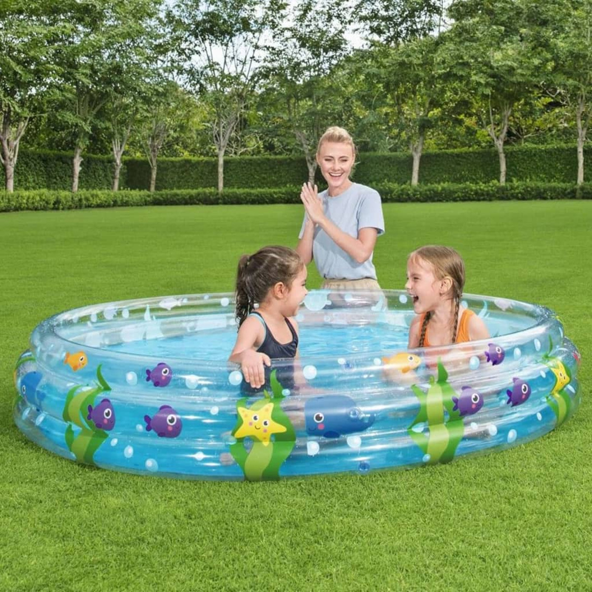 Kinder in einem Pool mit einer klatschenden Frau. Grünes Gras und Bäume im Hintergrund.