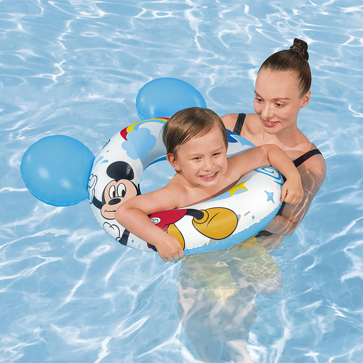 Eine Frau und ein Kind in einem Schwimmbad benutzen einen Mickey Mouse Schwimmring. Das Kind lächelt.