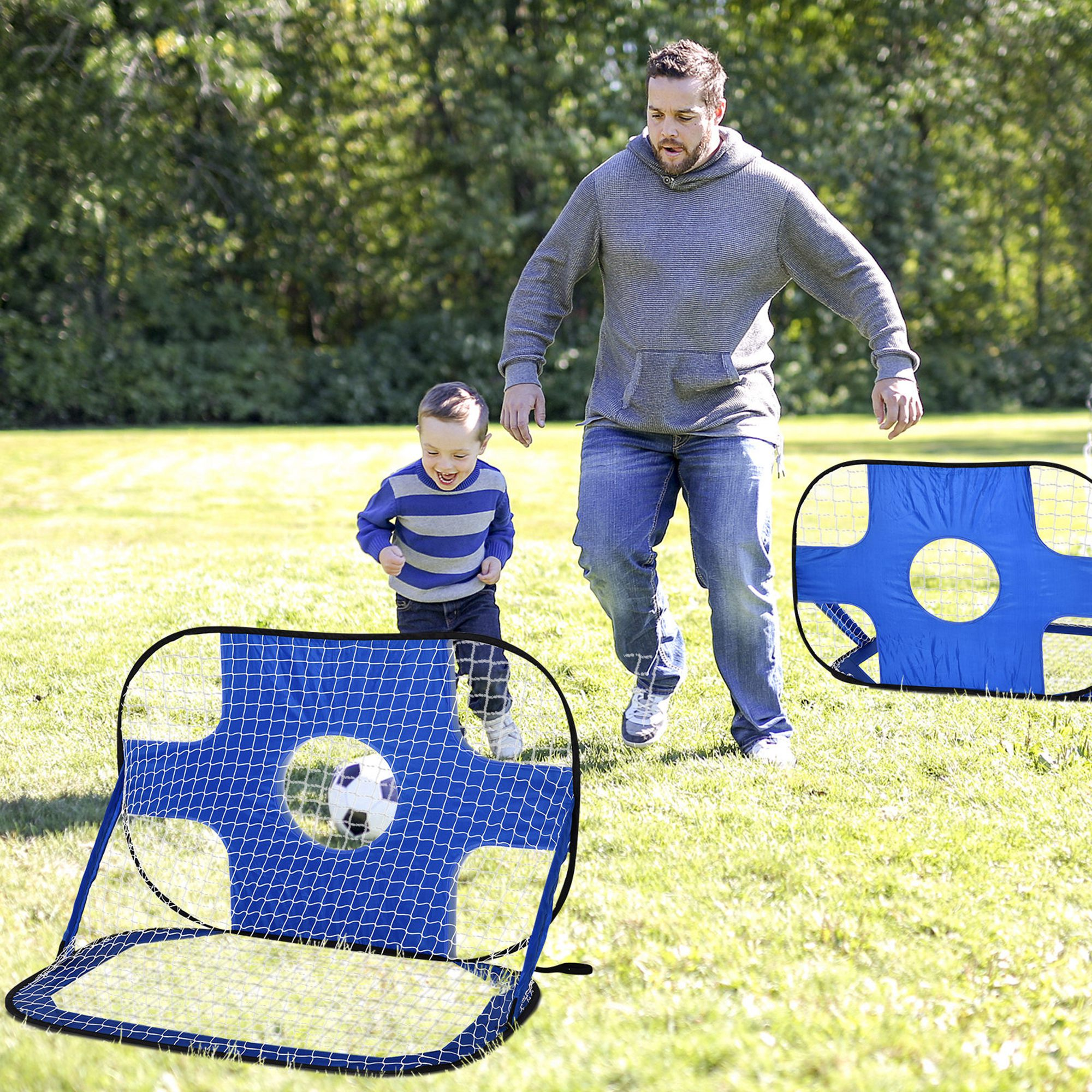 Ein Mann und ein Junge spielen Fußball. Der Junge schießt einen Fußball ins Tor. Grünes Gras und blaue Tore sind vorhanden.
