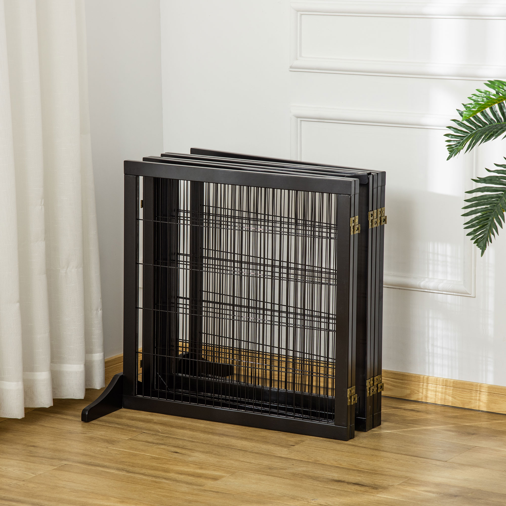 Ein zusammengeklappter schwarzer Hundeauslauf mit Metallgitter, vor einer weißen Wand und Holzboden.