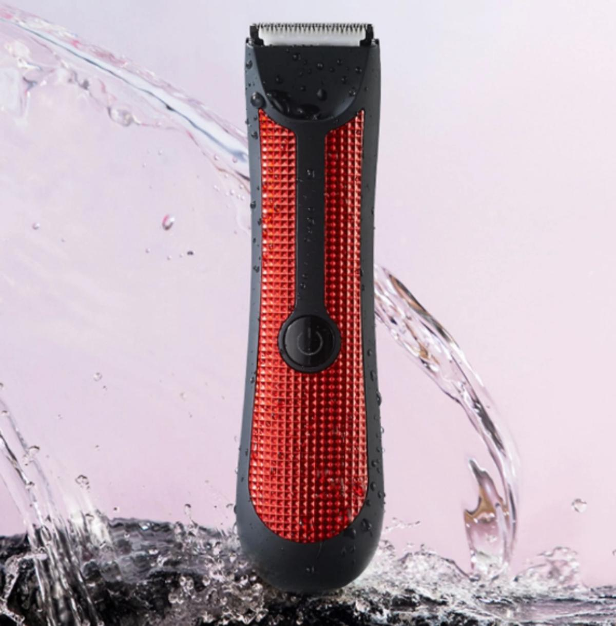 Ein schwarzer und roter elektrischer Rasierer mit spritzendem Wasser auf rosa Hintergrund.
