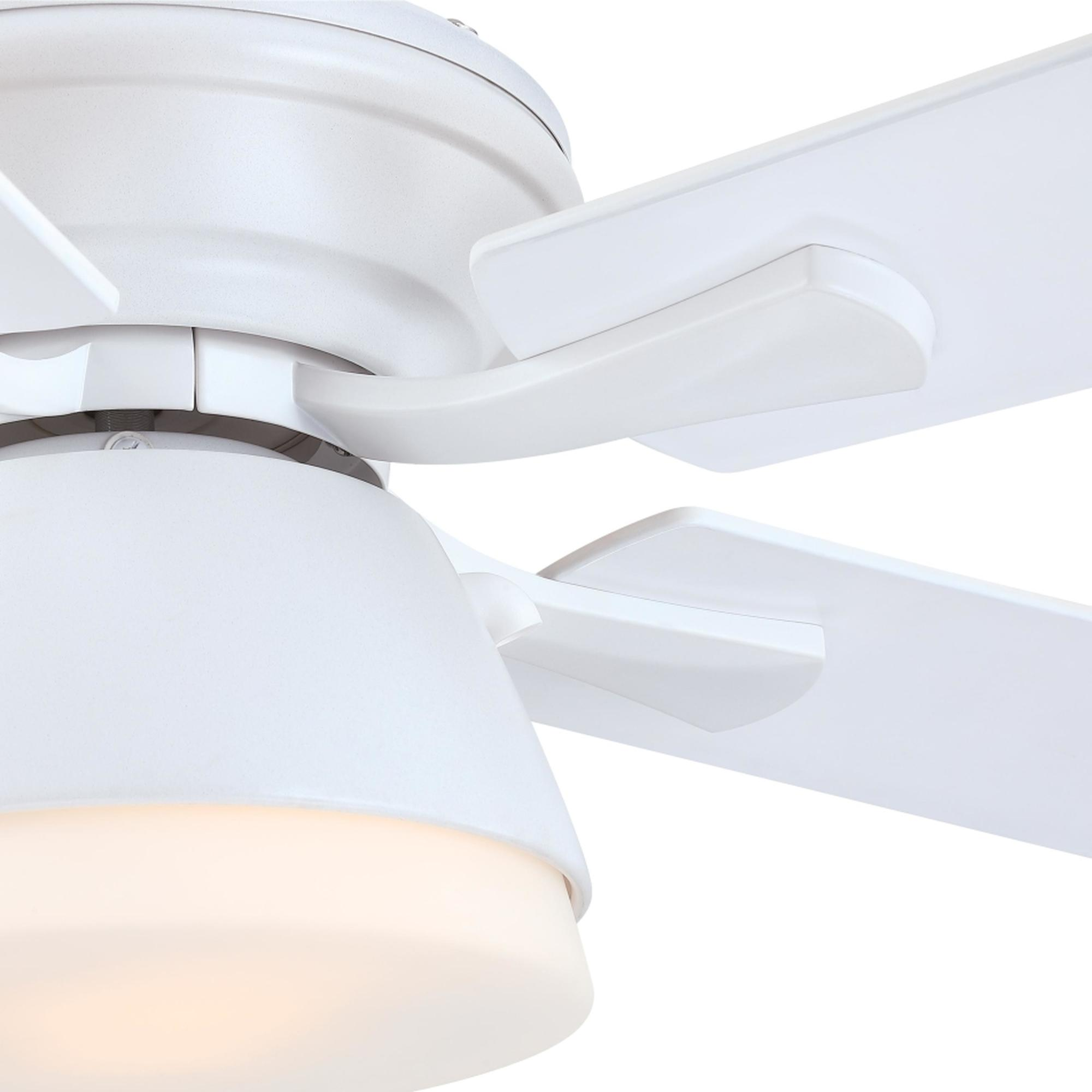 Nahaufnahme eines weißen Deckenventilators. Fokus auf die Leuchte, mit Blättern im Hintergrund.