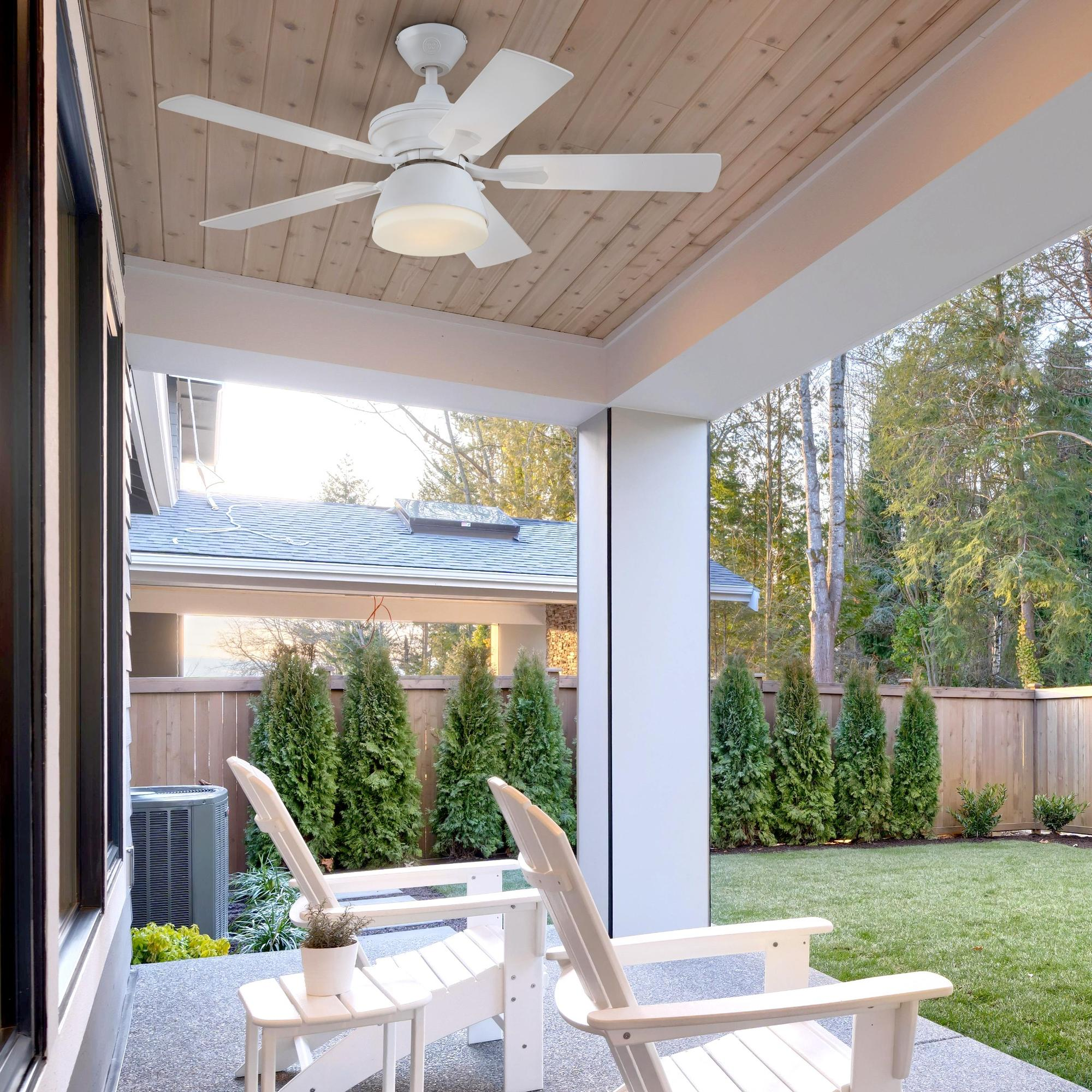 Ein weißer Deckenventilator mit fünf Flügeln ist an einer Holzveranda-Decke montiert.