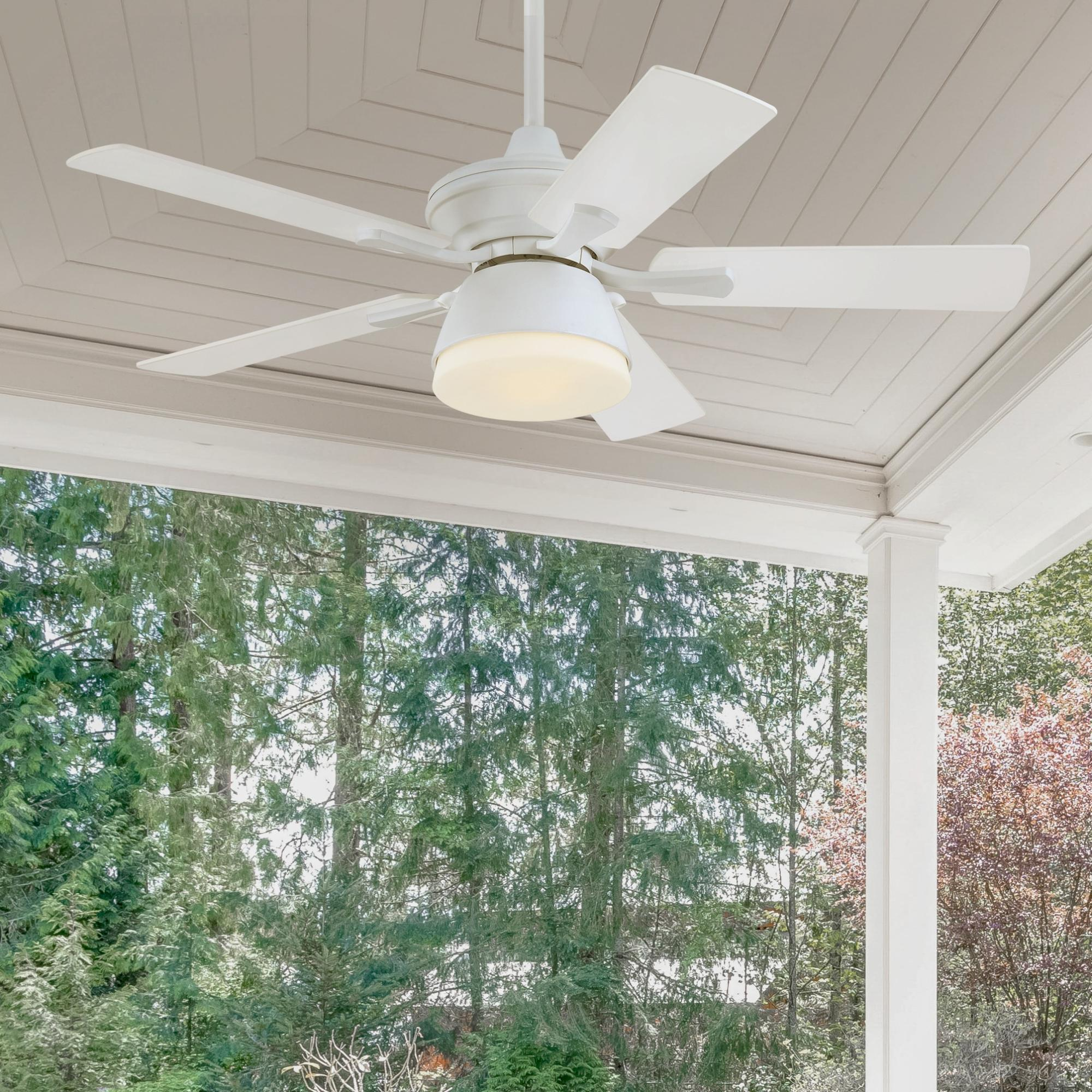 Weißer Deckenventilator mit Flügeln, an einer Veranda montiert. Grüne Bäume füllen den Hintergrund.