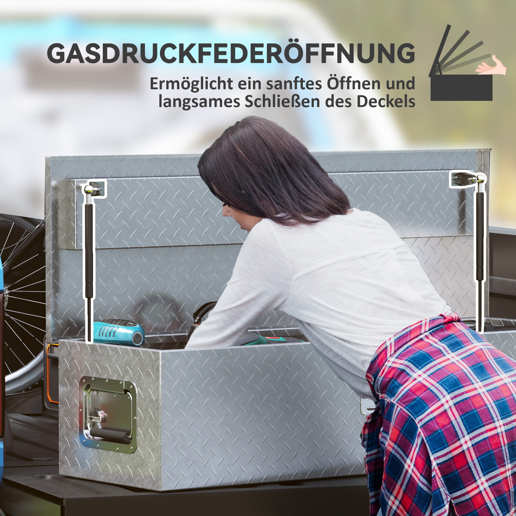 Eine Frau öffnet eine Metall-Aufbewahrungsbox. Die Box hat ein Rautenmuster und befindet sich auf einer Ladefläche.