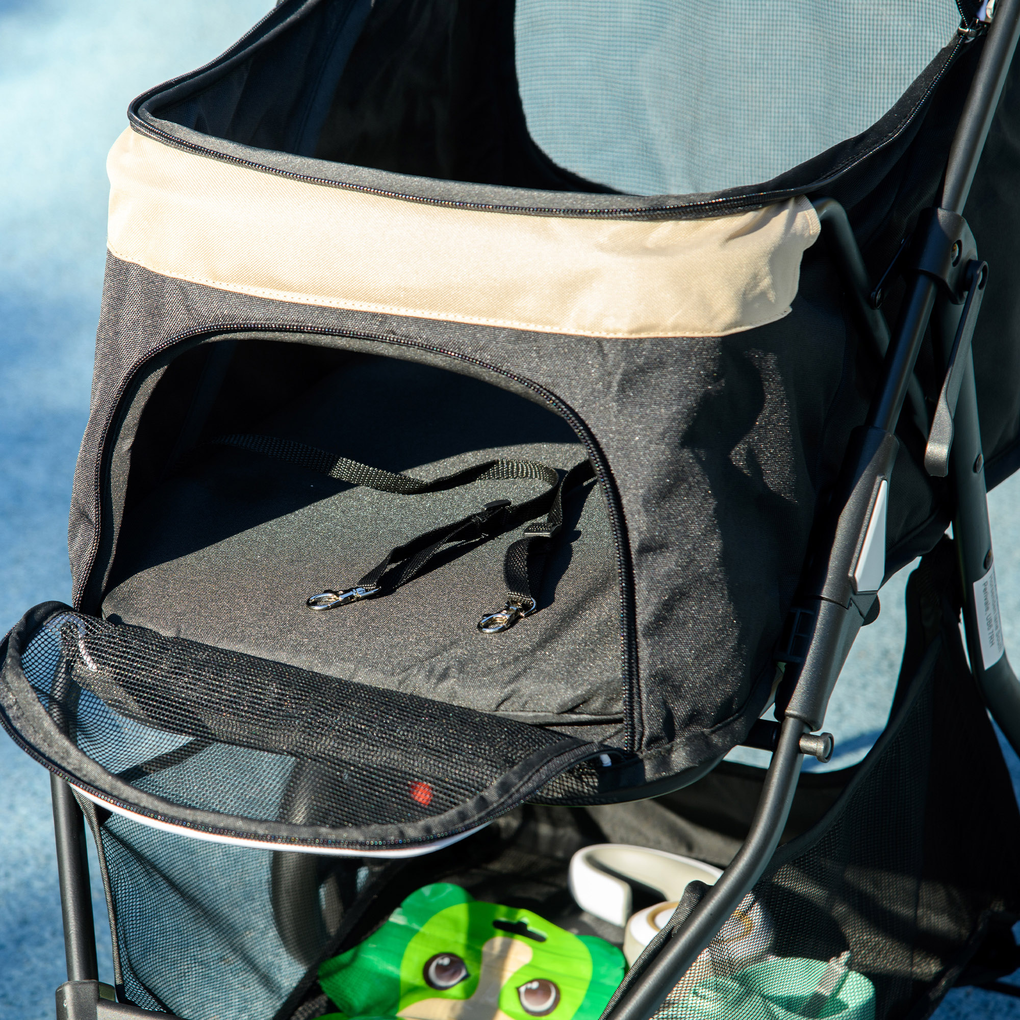 Nahaufnahme des Innenraums eines Haustier-Kinderwagens. Schwarzer Stoff, Mesh und ein grünes Spielzeug sind sichtbar.