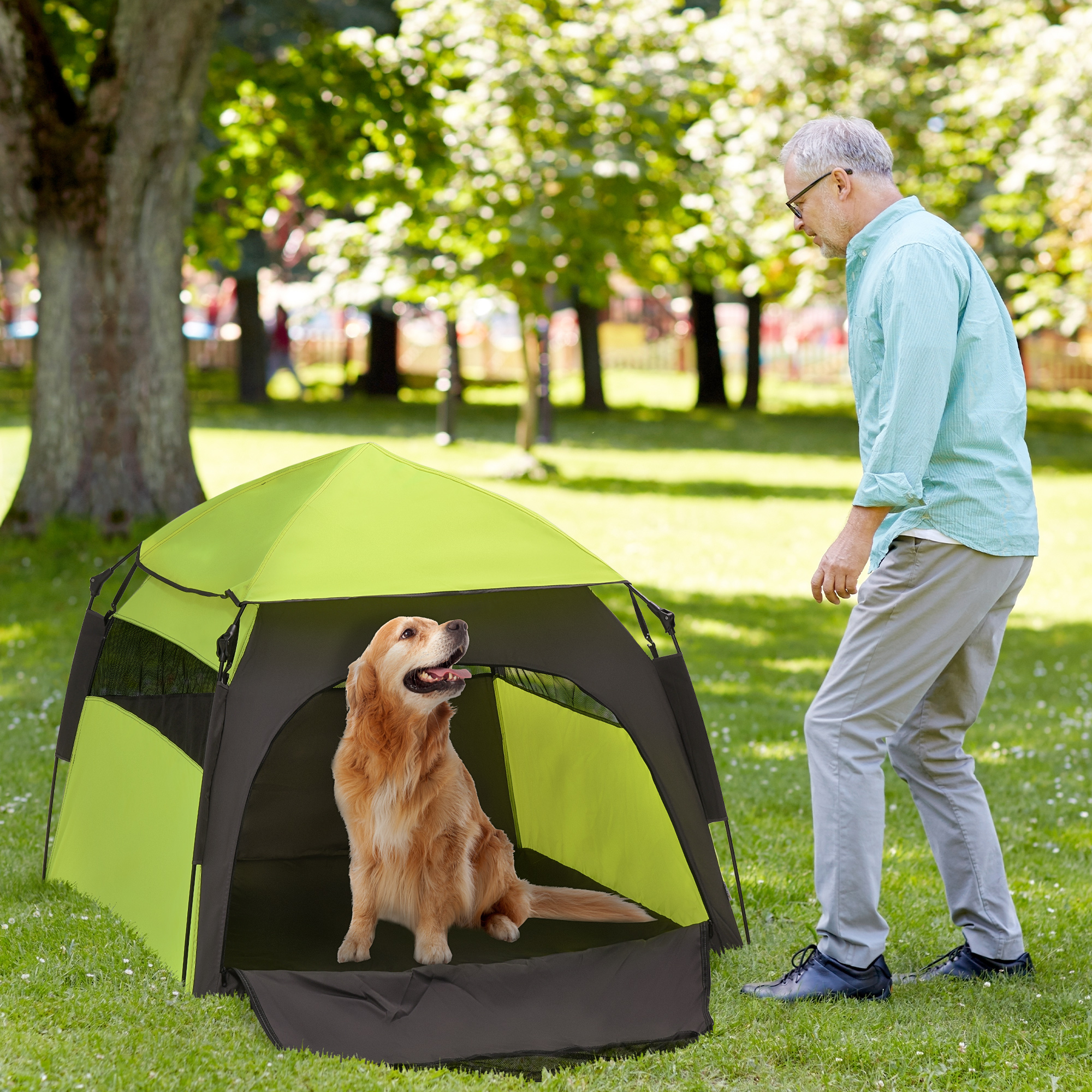 Mann und Hund in einem grün-schwarzen Hundezelt auf einer Wiese.