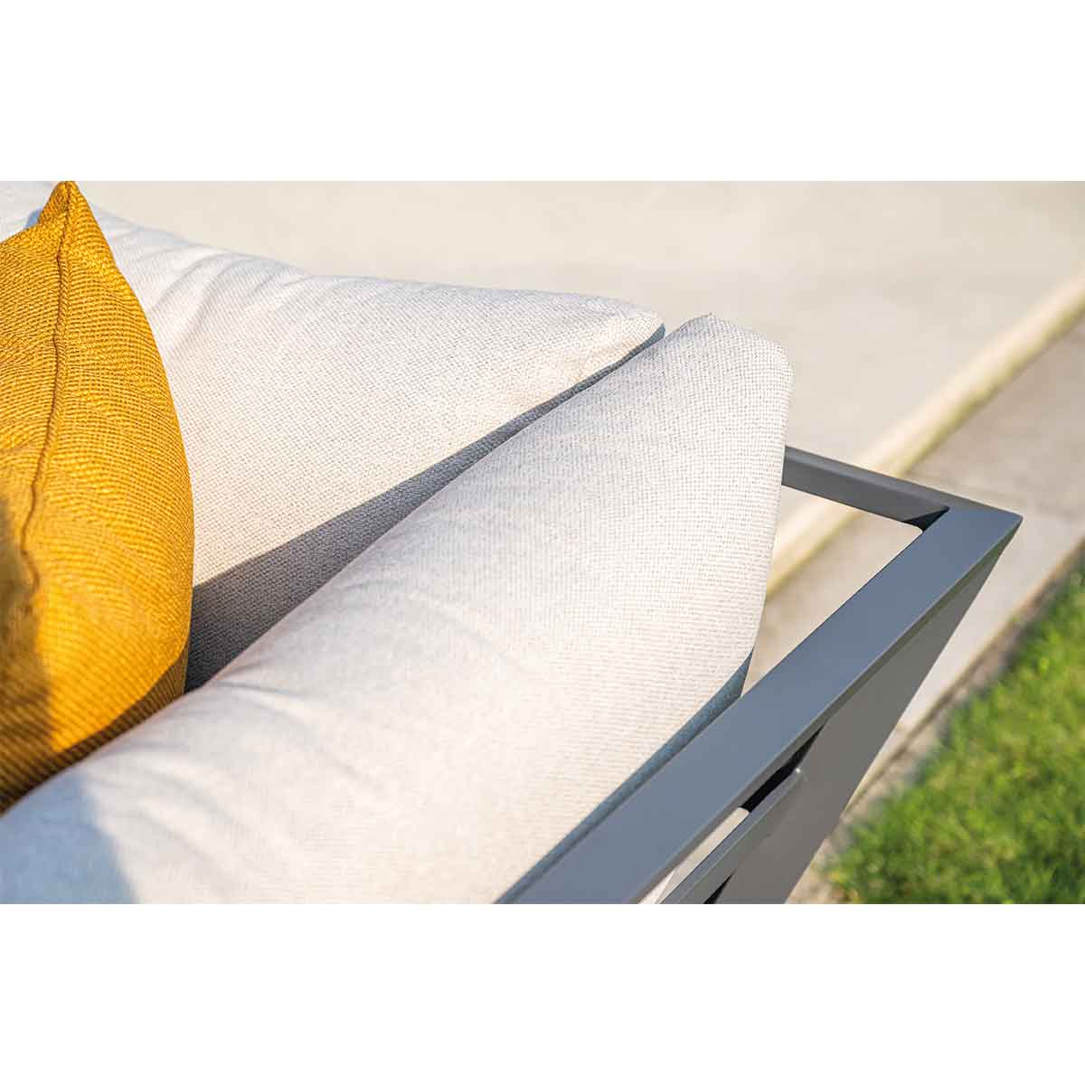 Coussins de canapé d'extérieur, jaunes et blancs, sur un cadre gris, avec de l'herbe verte visible.