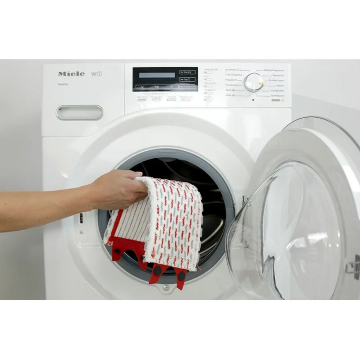Una mano che inserisce un panno bianco e rosso in una lavatrice Miele bianca.