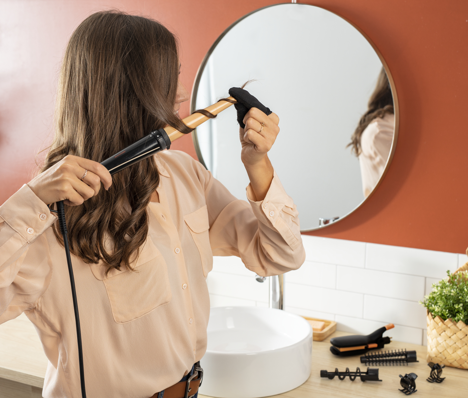 Una donna si arriccia i capelli con un arricciacapelli nello specchio del bagno.