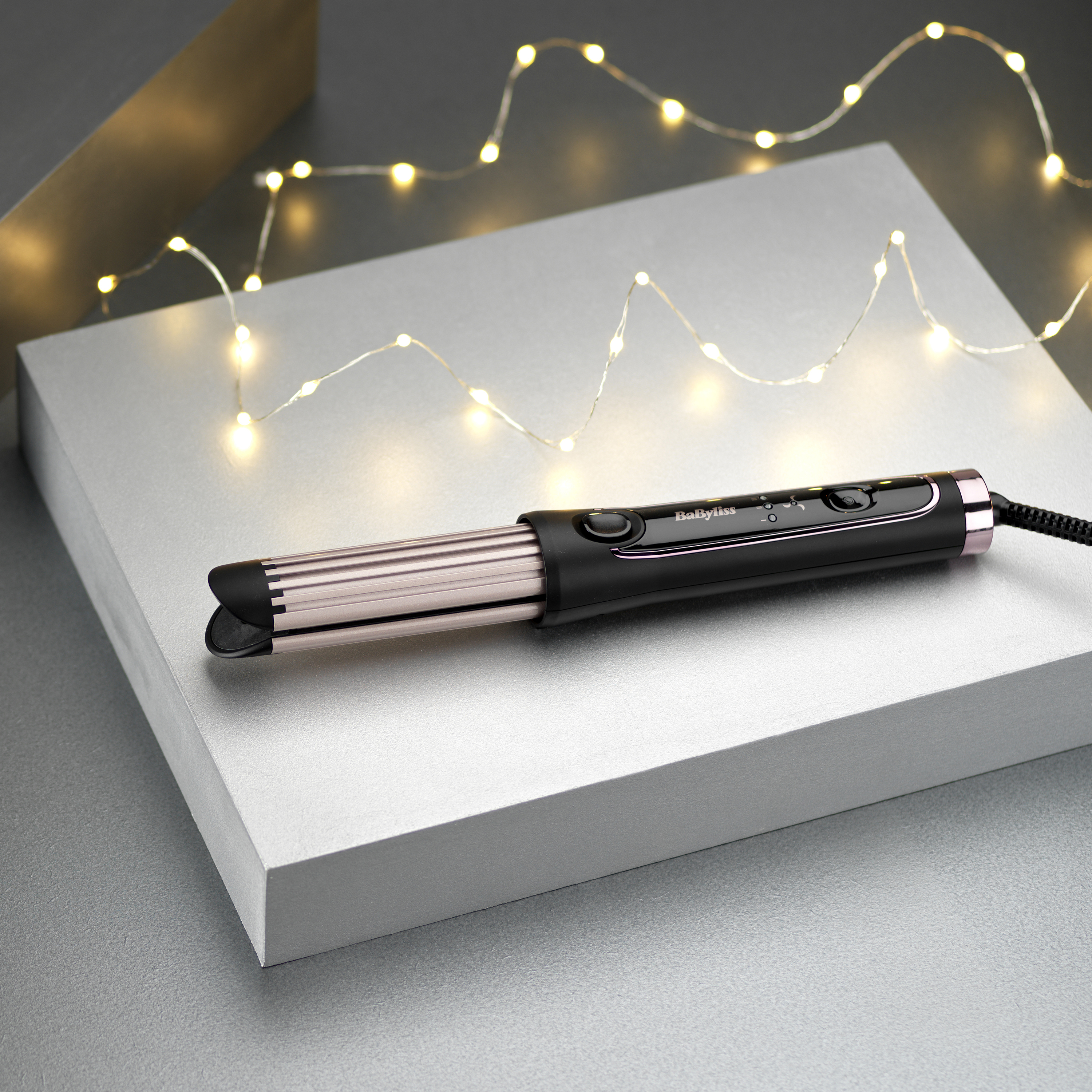 Ein Kräusel-Haarstyling-Tool auf einem grauen Block. Lichter im Hintergrund.