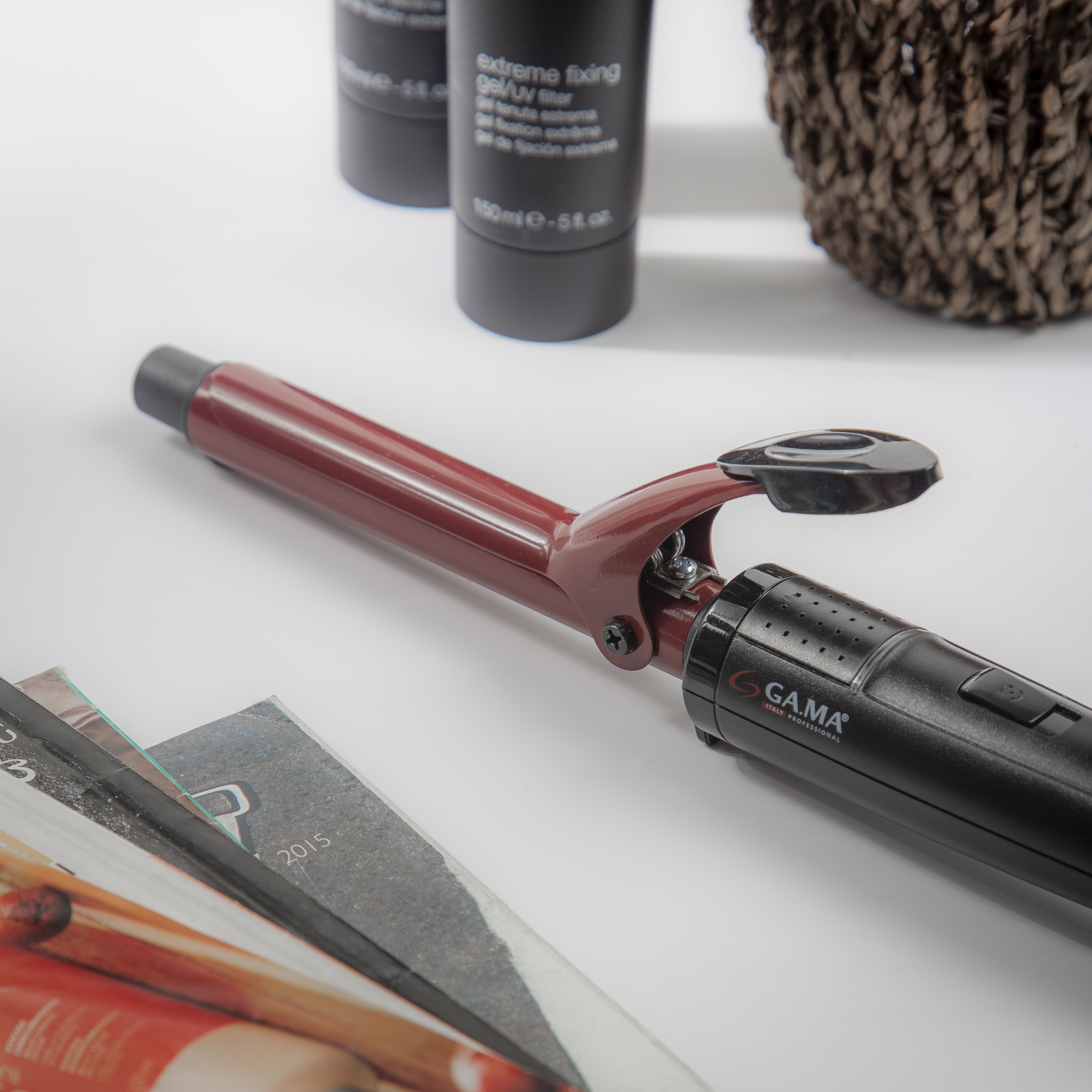 Arricciacapelli rosso e nero con accessori e rivista su una superficie bianca.
