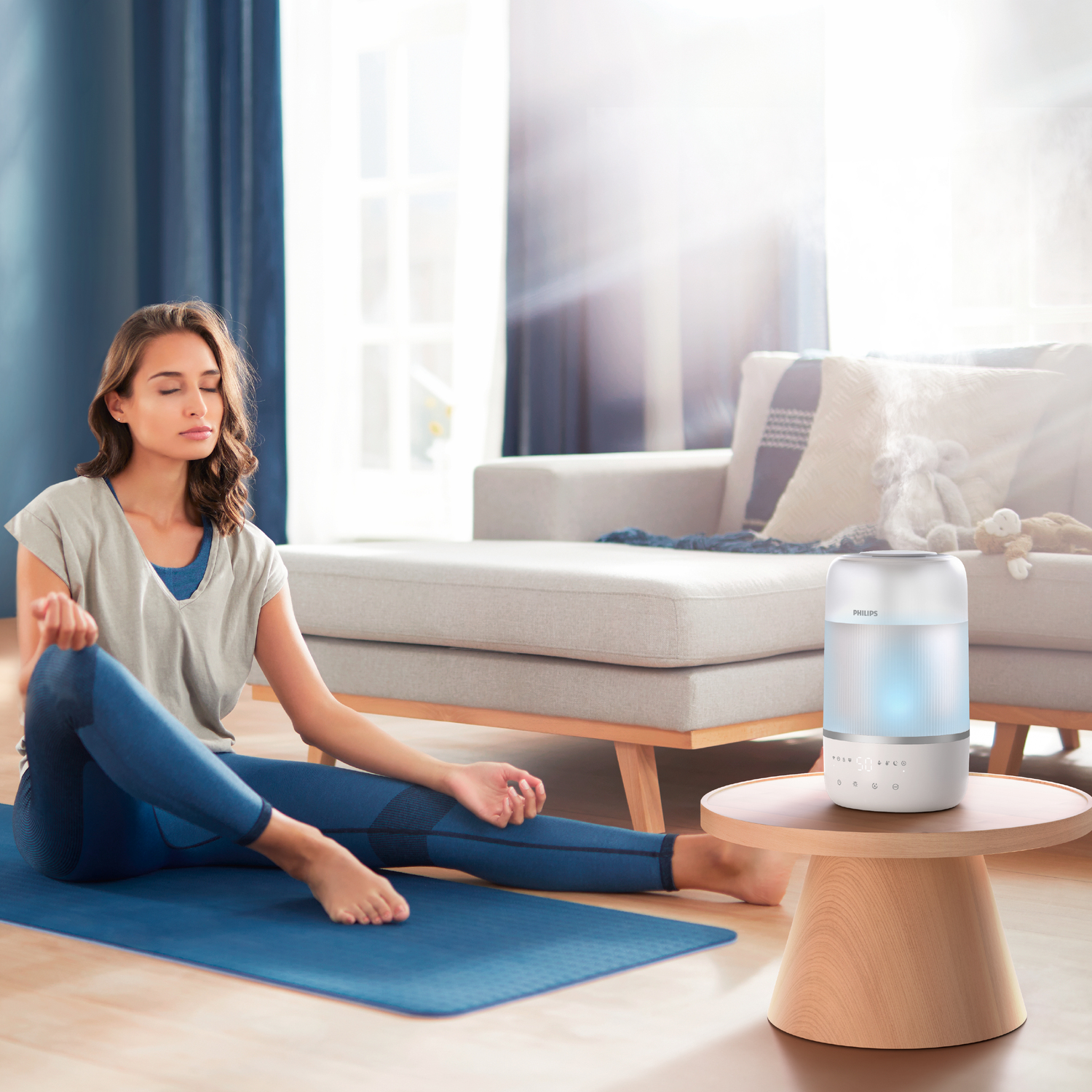 Ahşap bir masada Philips aroma yayıcı ile yoga matında meditasyon yapan kadın.