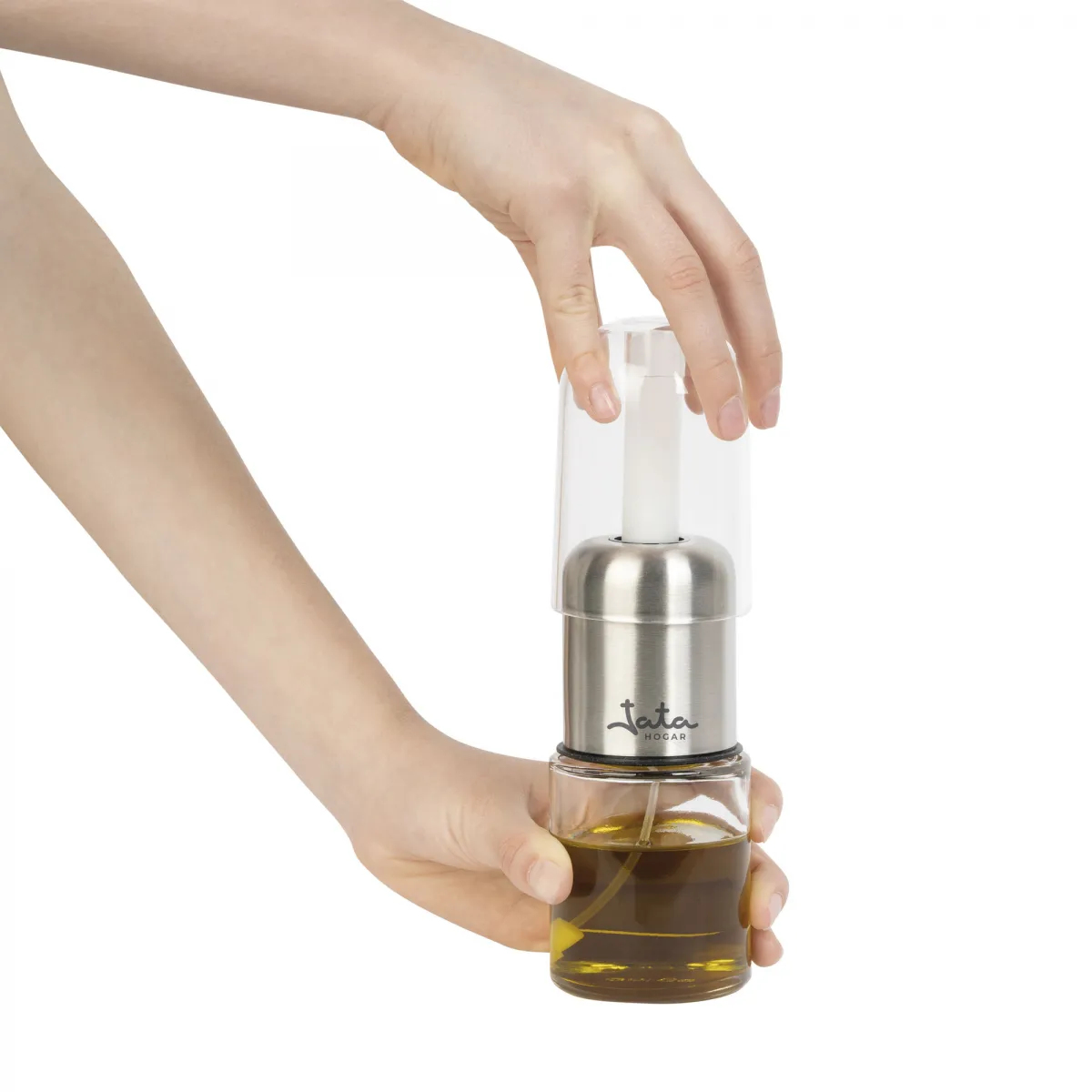 Manos sostienen una botella de vidrio con aceite y un pulverizador. Una tapa transparente está encima.