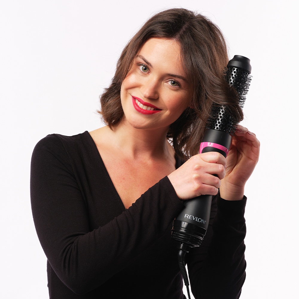 Kobieta używa suszarki do włosów Revlon. Suszarka jest czarna i różowa. Uśmiecha się do kamery.