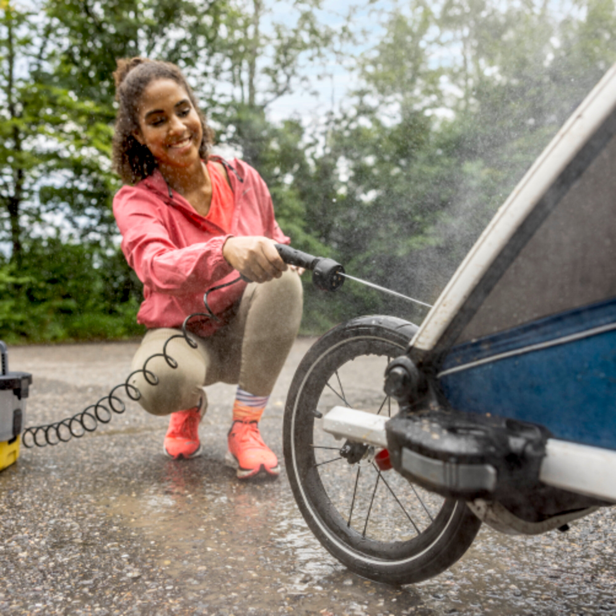 Een vrouw die een kinderwagen bespuit met een slang op een natte bestrating.