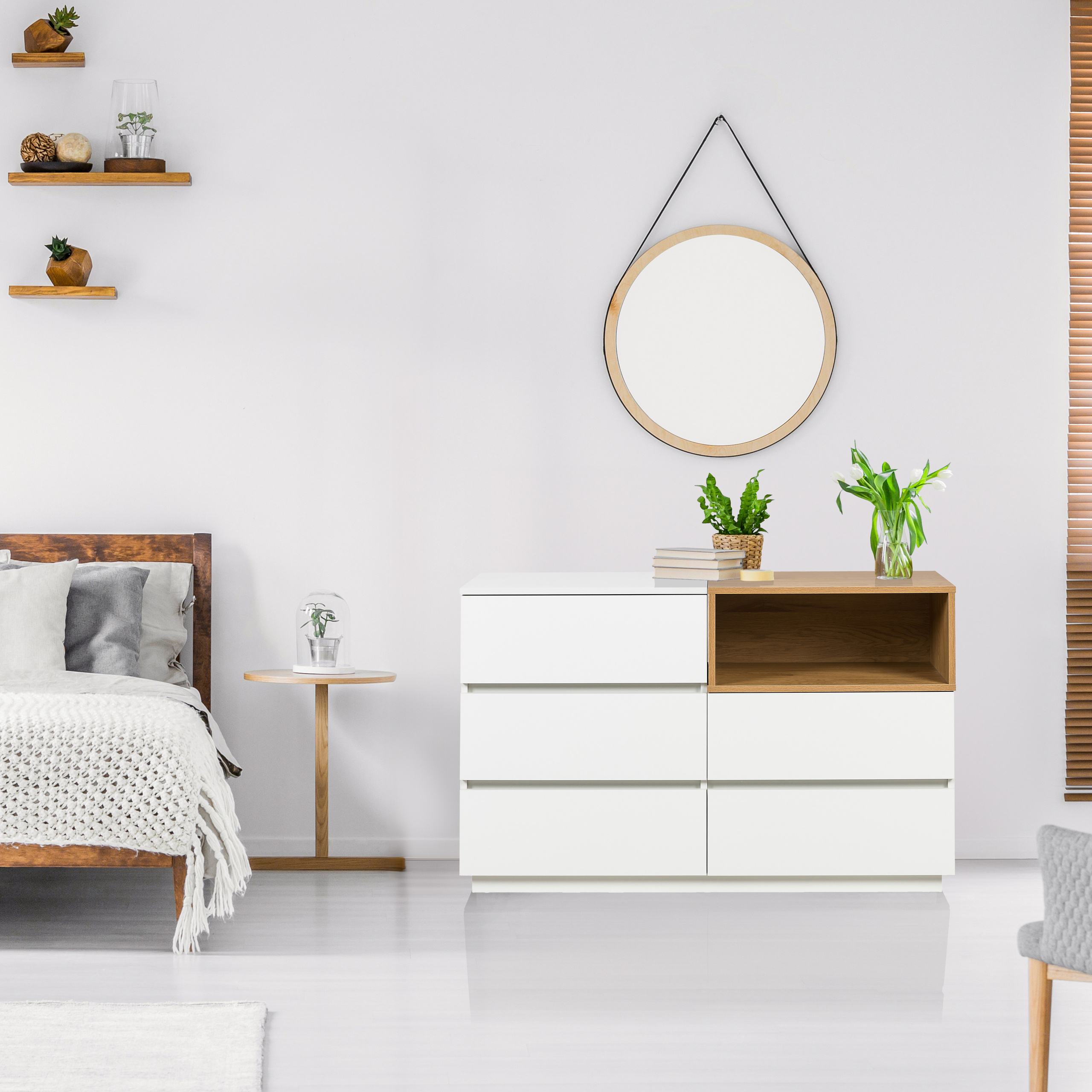 Schlafzimmer mit weißen Wänden, Holzbett, Kommode, Spiegel und Regalen.