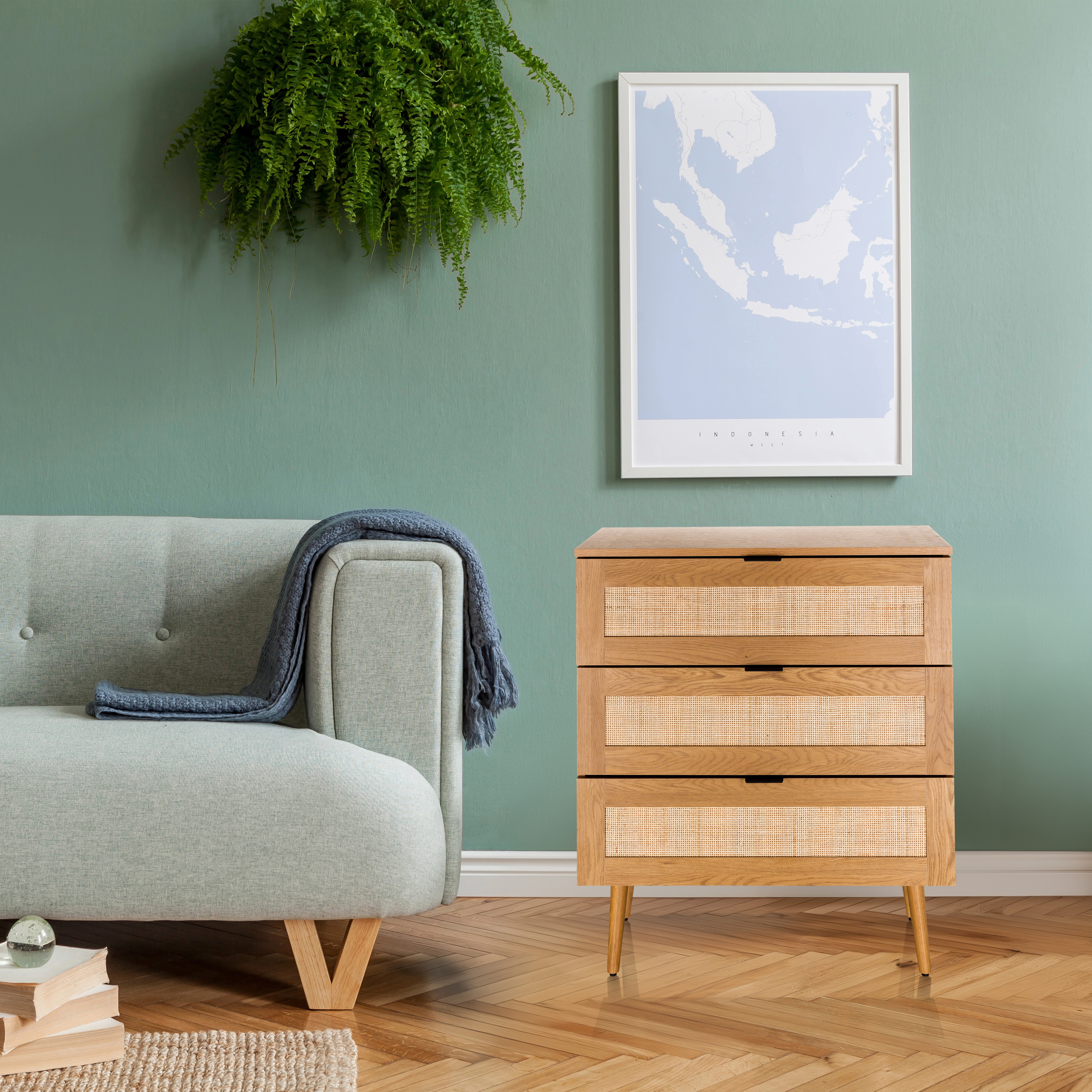 Ein Holzschrank mit drei Schubladen, ein blauer Überwurf, ein Sofa, ein Farn und eine gerahmte Karte.