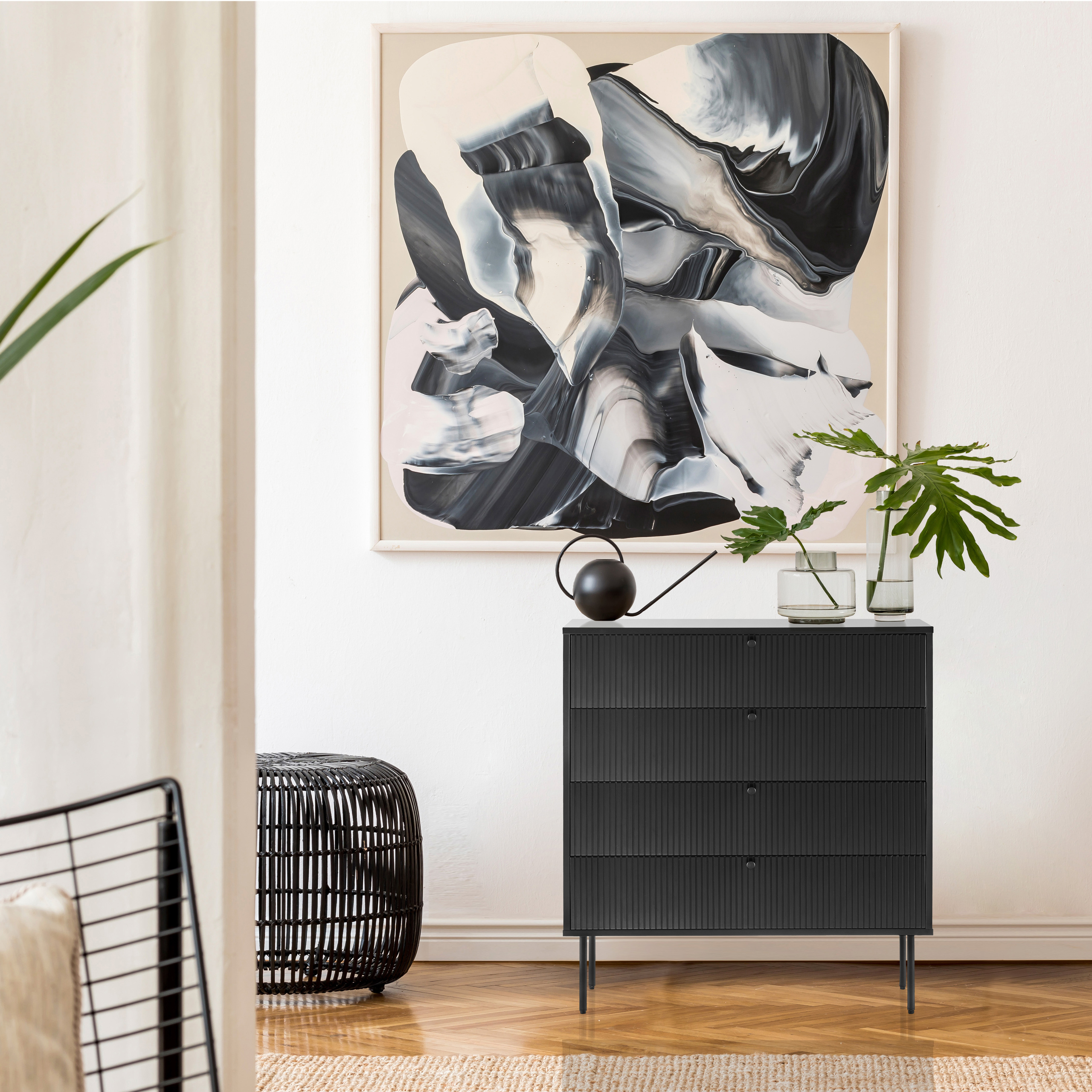 Schwarze Kommode mit Gemälde, Pflanze und gewebtem Hocker.
