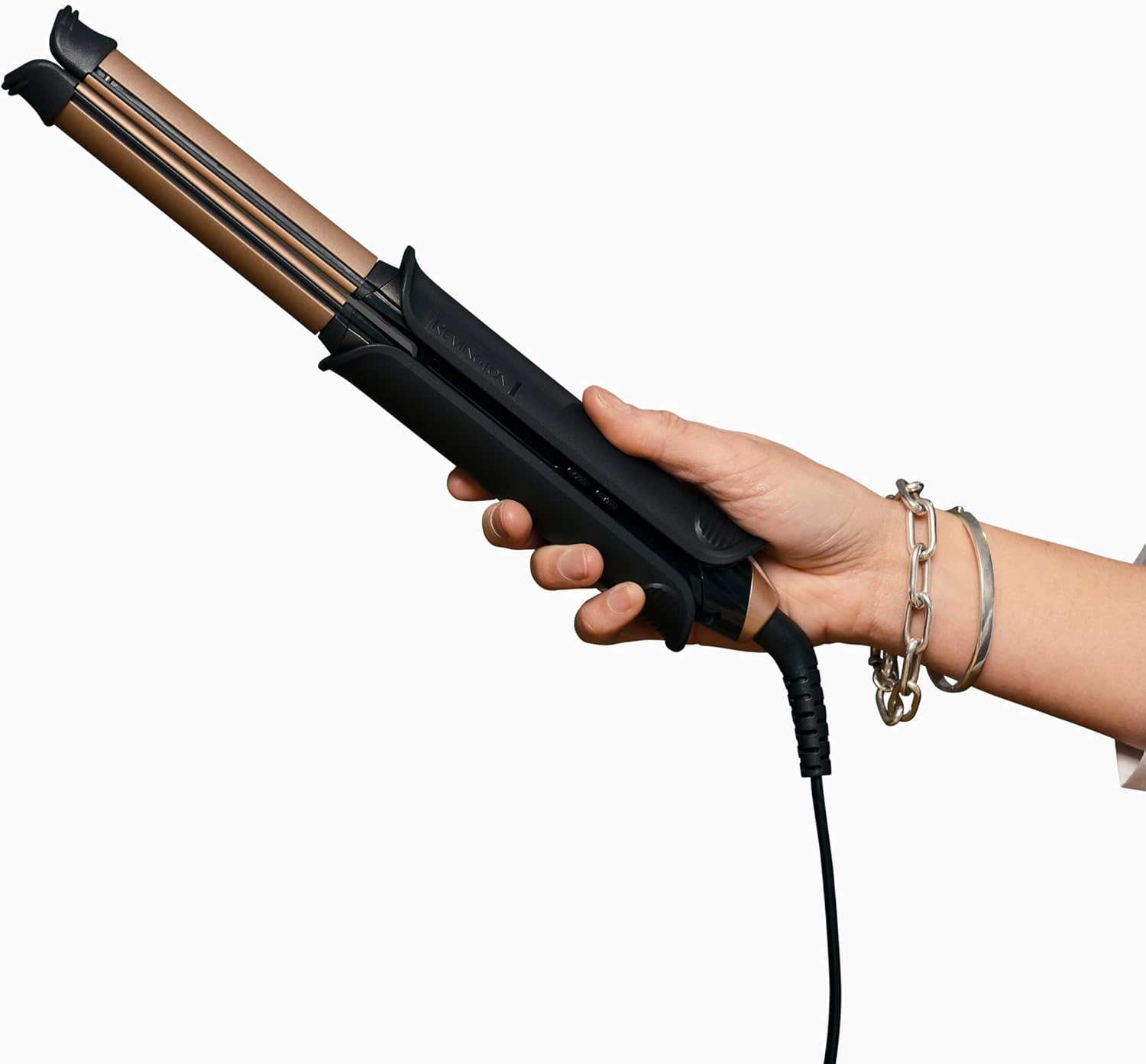 Die Hand einer Person hält einen schwarzen und goldenen Haarglätter. Silberne Armbänder sind am Handgelenk.