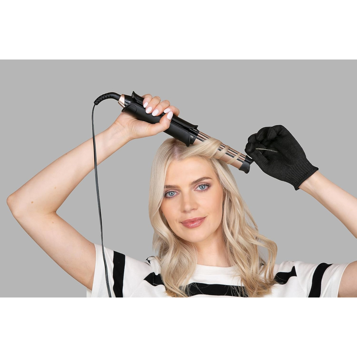 Eine Frau lockt ihr Haar mit einem Lockenstab und Handschuh.