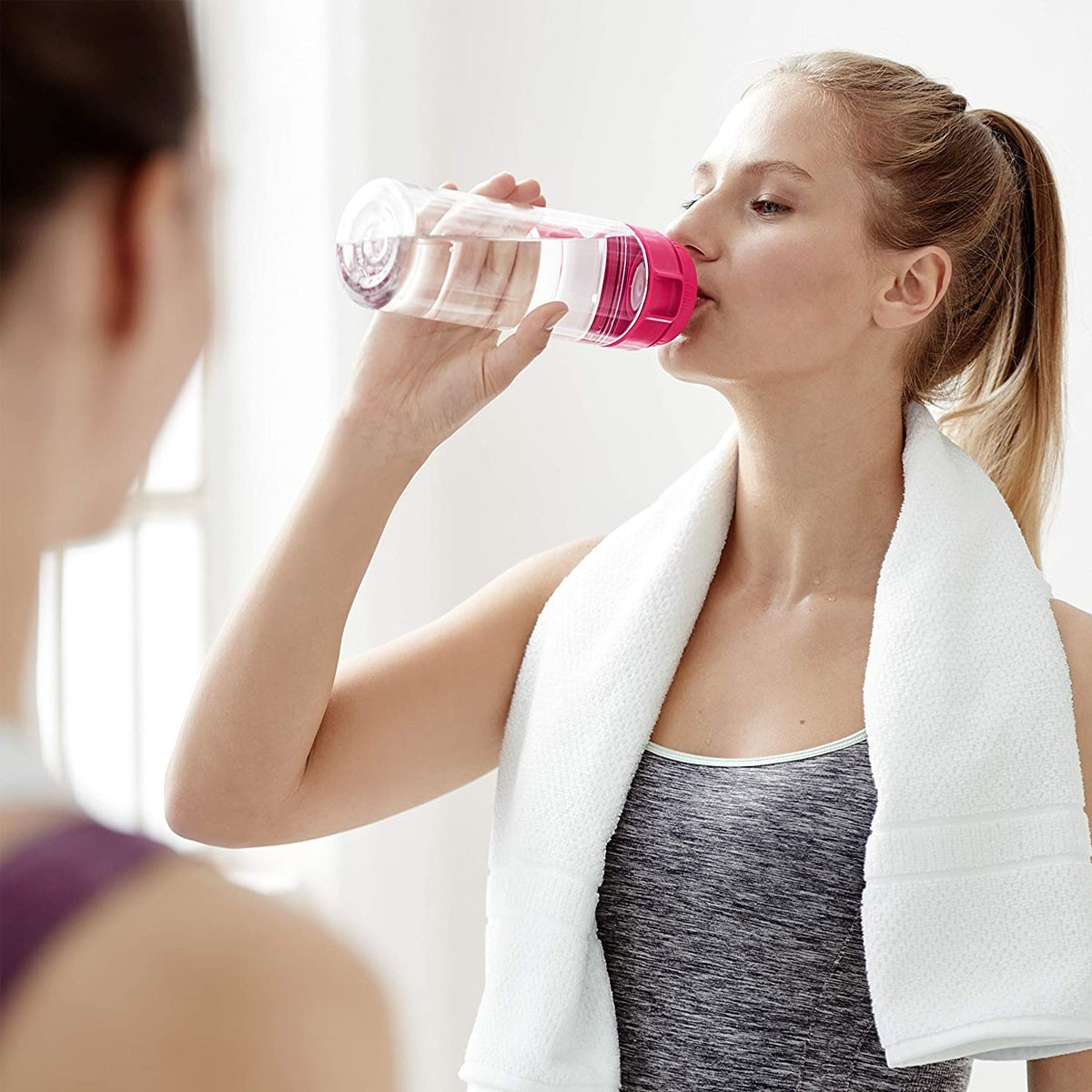 Donna che beve da una bottiglia d'acqua, un'altra persona sullo sfondo.