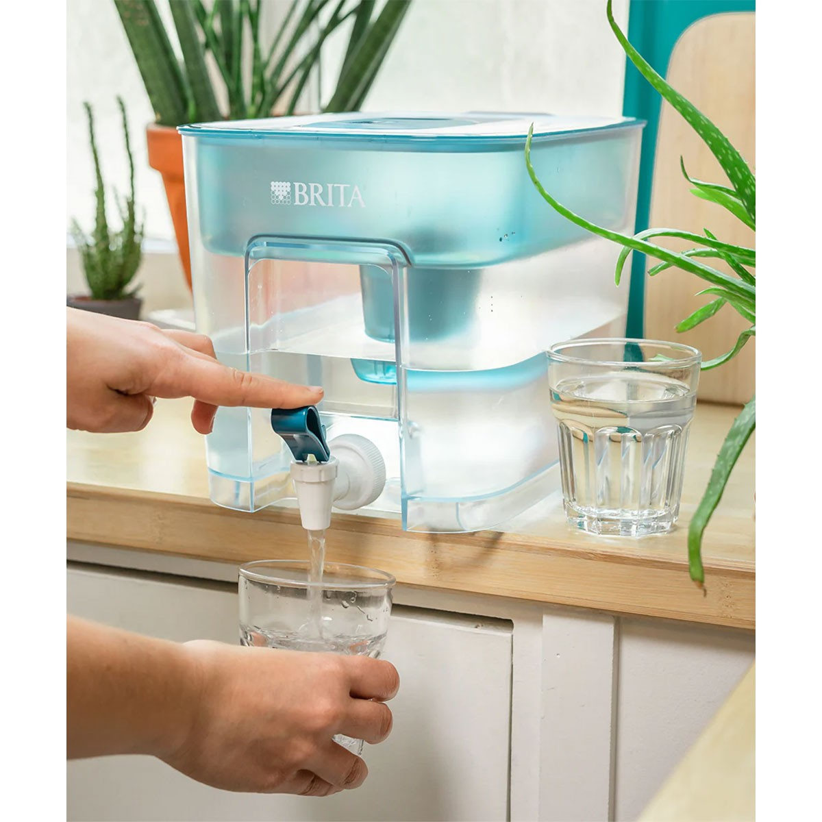 Ręka nalewa wodę z dystrybutora wody Brita do szklanki.