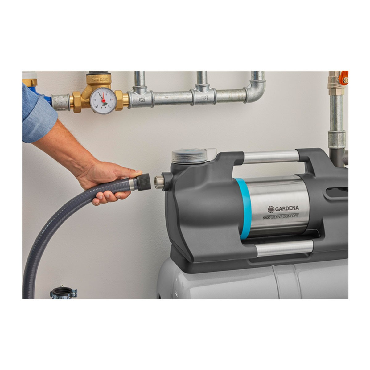 Osoba podłączająca wąż do pompy wodnej, na tle ściany i rur.