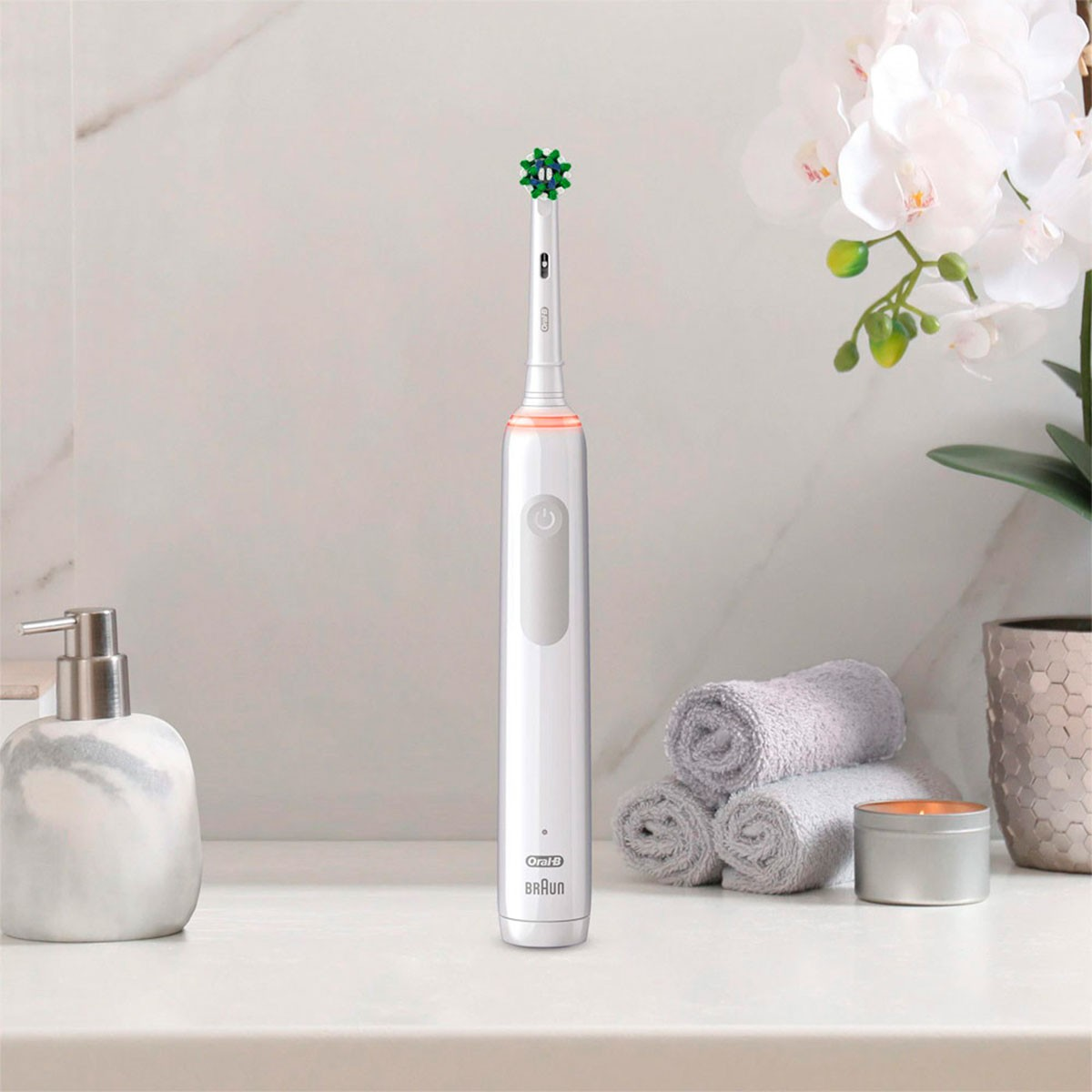 Weiße elektrische Zahnbürste mit grünem Kopf auf einer Theke. Weitere Artikel: Seife, Handtücher und Blumen.