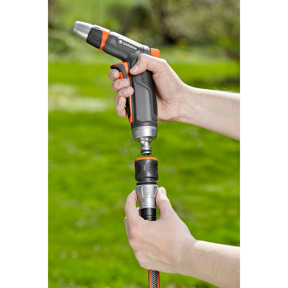 Manos conectan una boquilla de pulverización GARDENA gris y naranja a un conector de manguera negro.