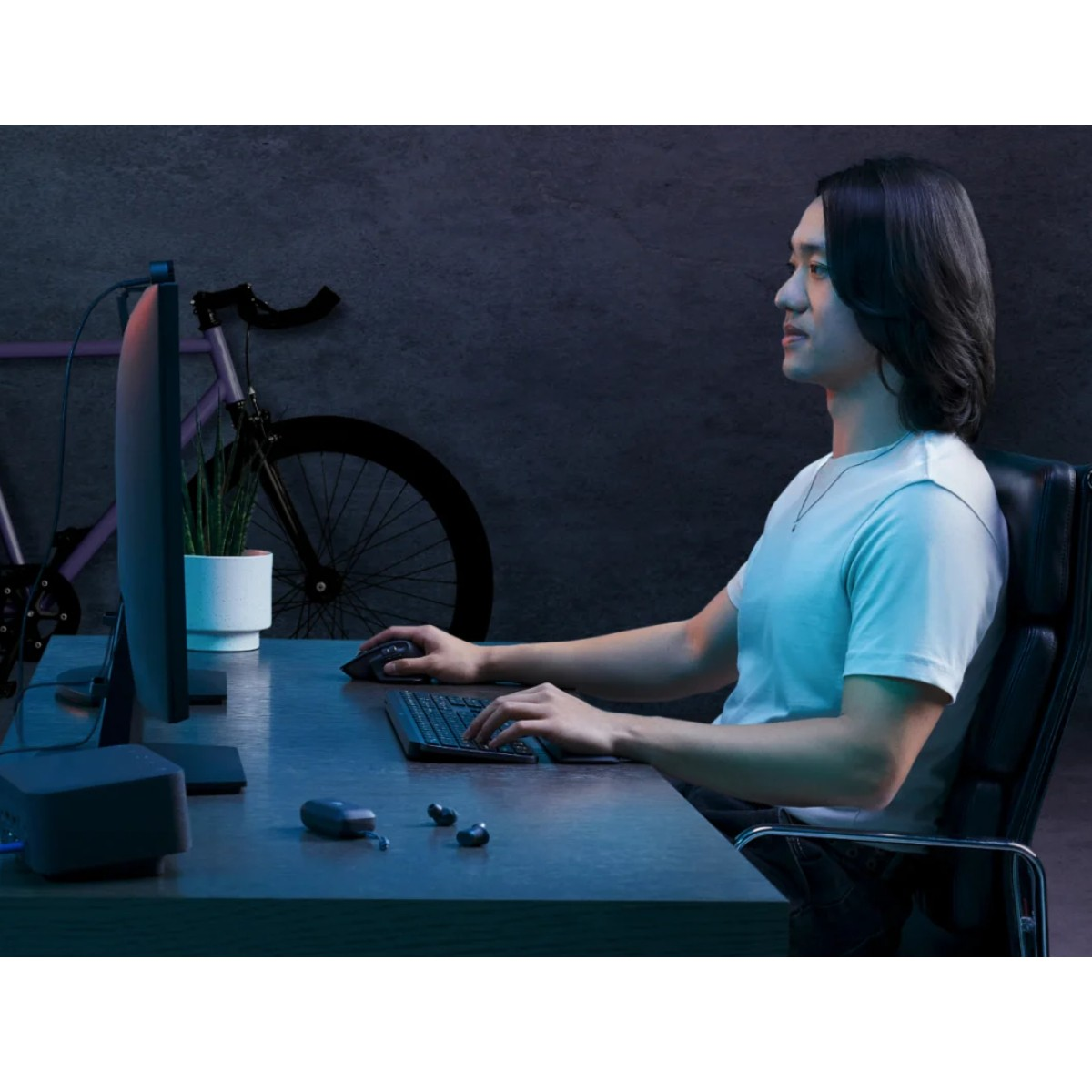 Mężczyzna używa klawiatury i myszy przy biurku przed monitorem. Rower i roślina w tle.