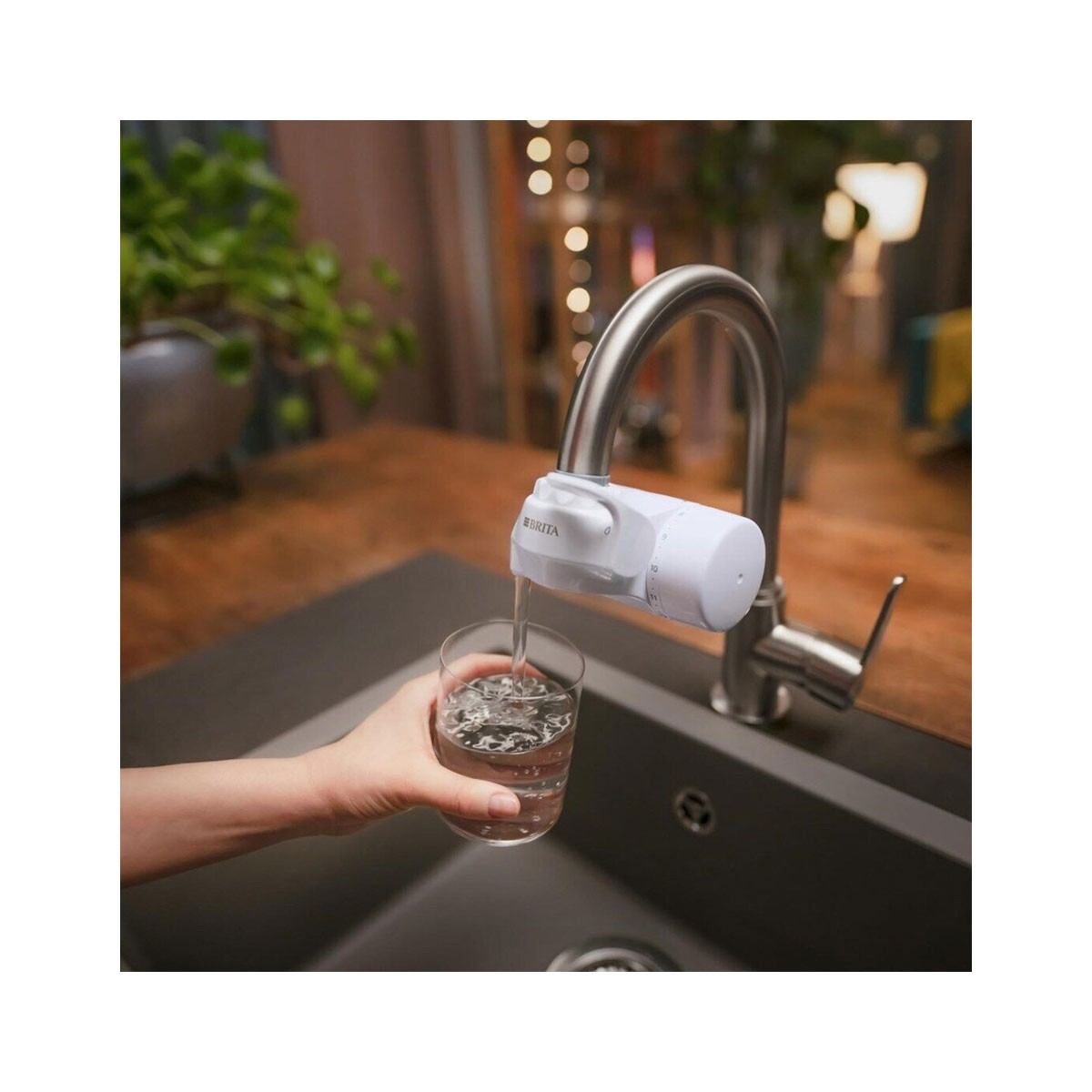 L'acqua scorre da un rubinetto in un bicchiere tenuto da una mano. Il rubinetto è bianco.