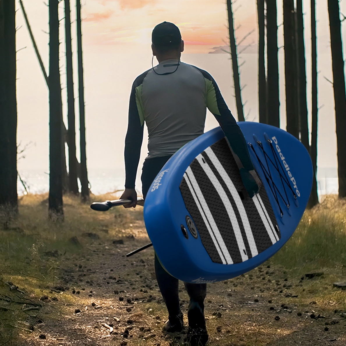 Man draagt een blauw paddleboard en peddel, lopend op een bospad.