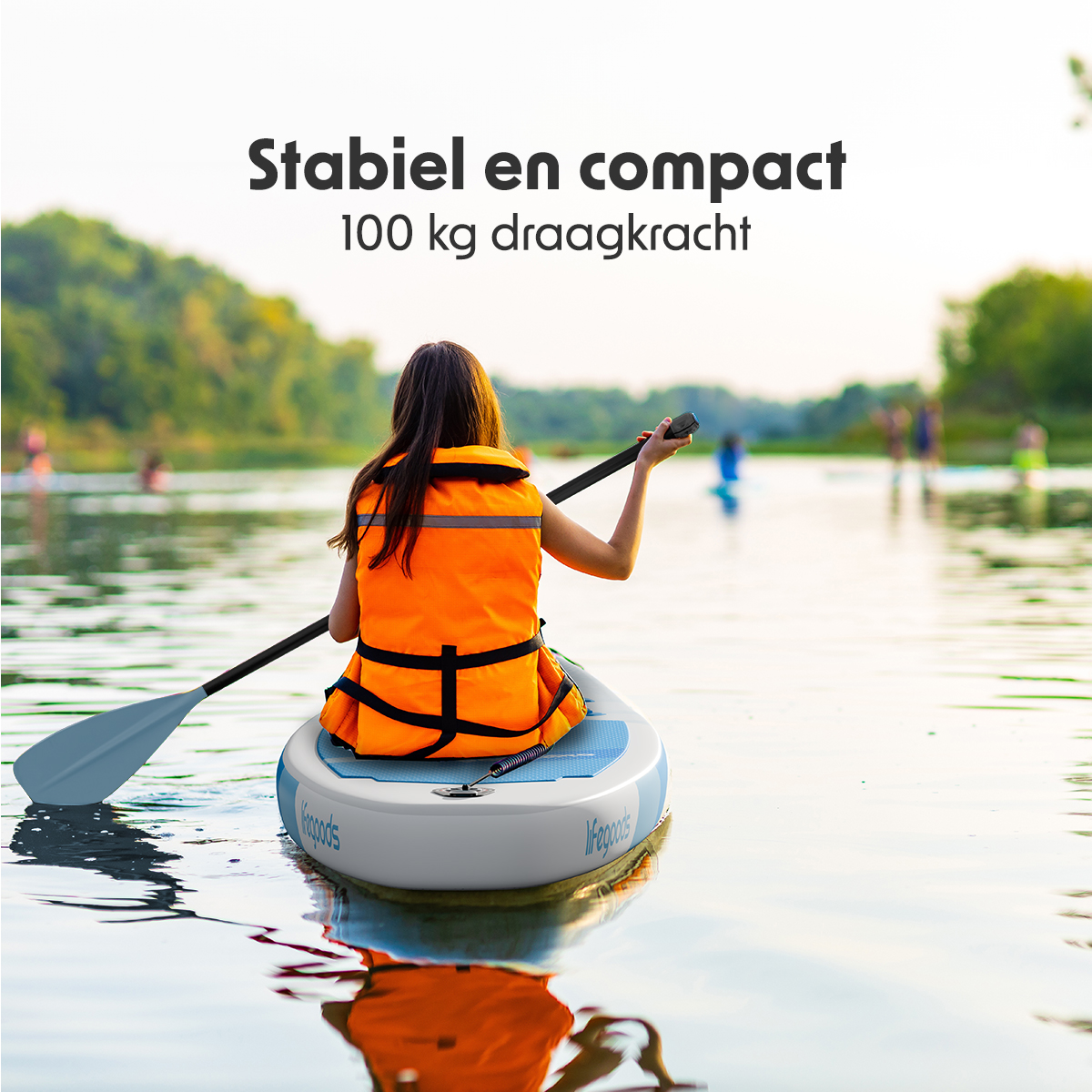 Femme sur une planche de SUP portant un gilet de sauvetage, faisant du paddle sur un lac. D'autres personnes sont en arrière-plan.