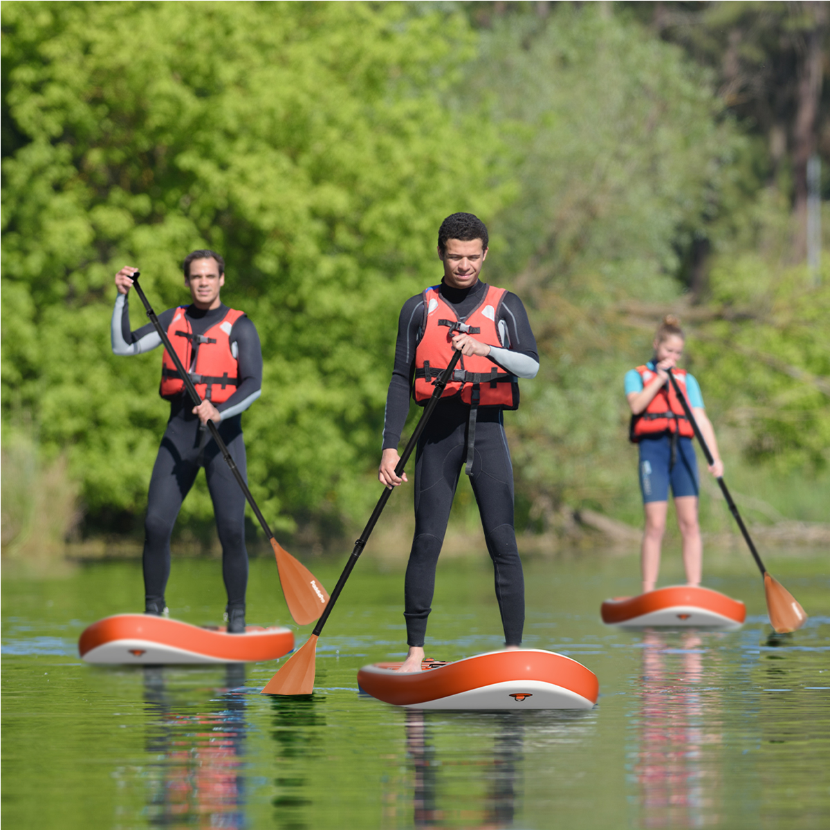Drie mensen suppen op een meer. Ze dragen zwemvesten en wetsuits.