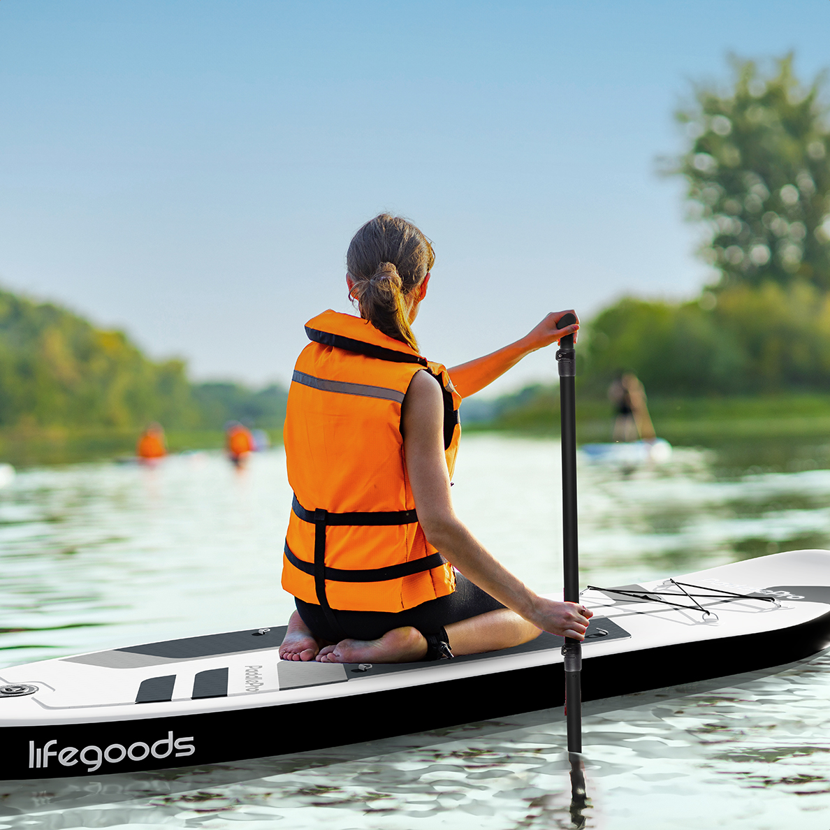Eine Frau in einer orangefarbenen Schwimmweste kniet auf einem SUP-Board und paddelt.