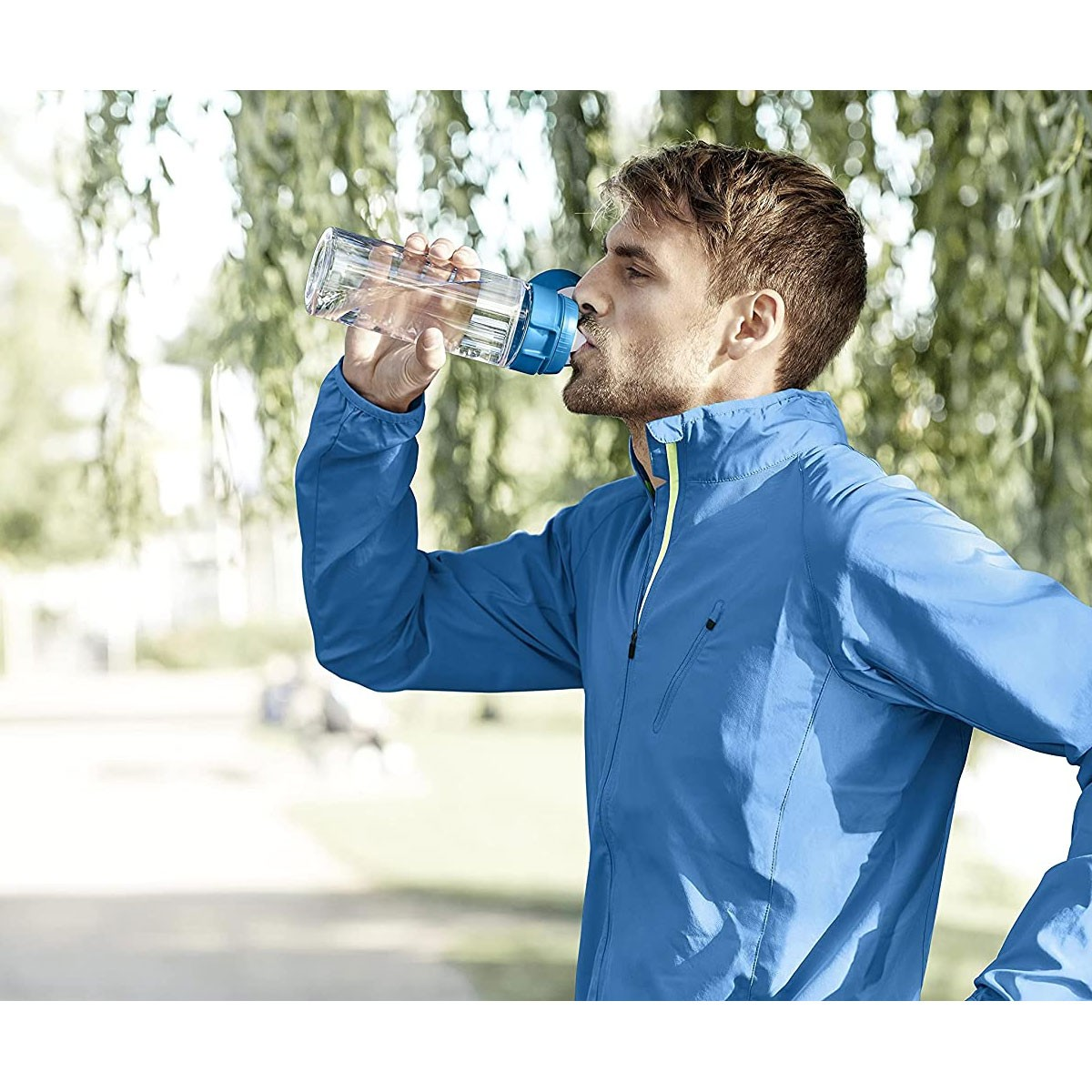 Mężczyzna pije wodę z przezroczystej butelki z niebieską zakrętką, na zewnątrz.