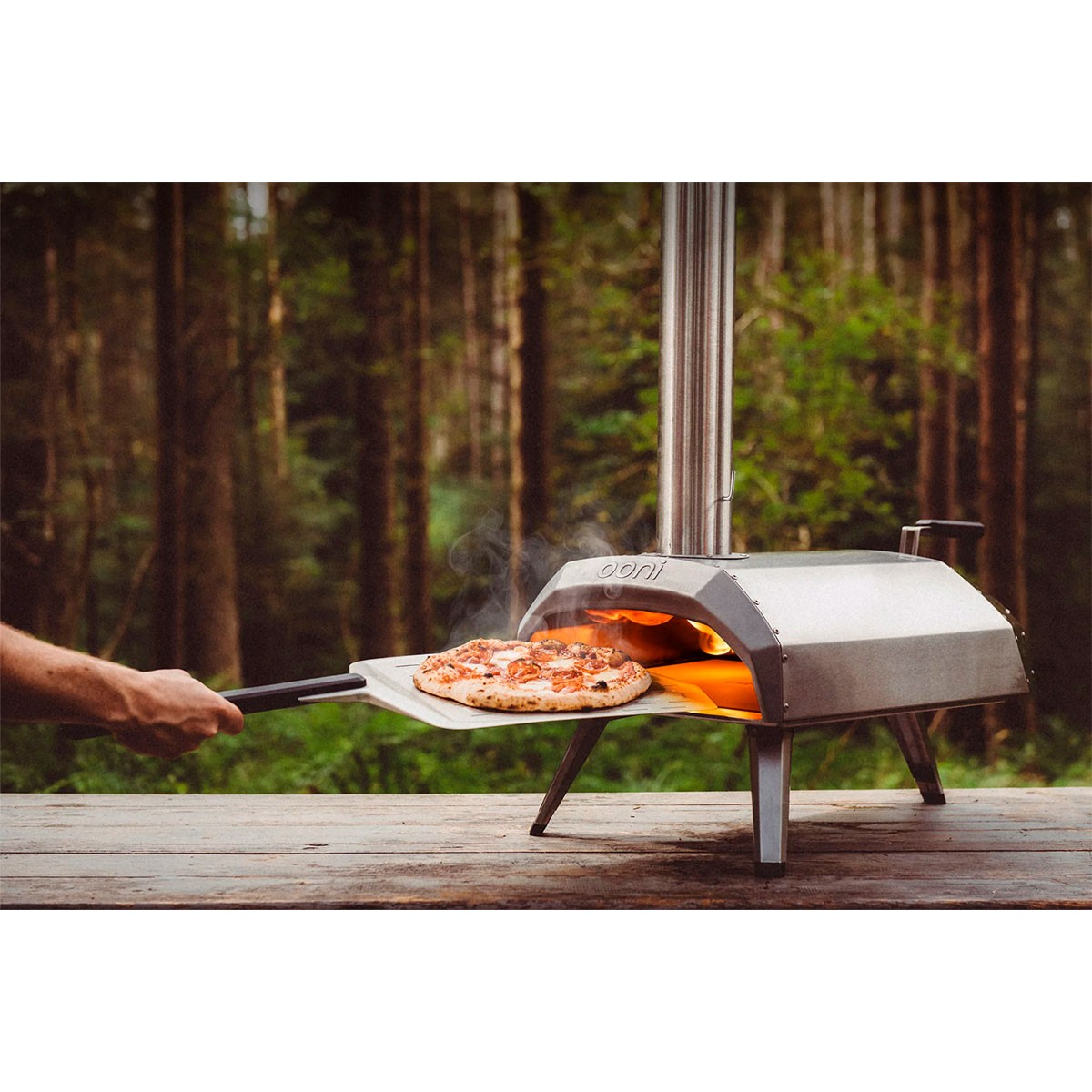 Una pizza viene rimossa da un forno per pizza. Il forno è su un tavolo di legno.